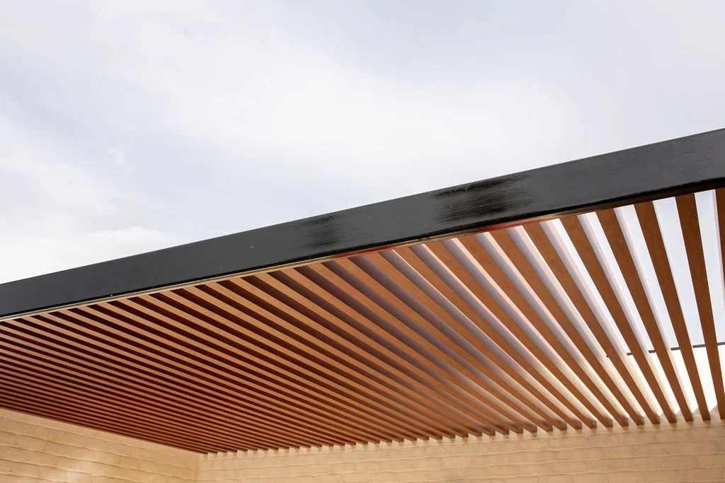 Close-up of a modern building's overhang with wooden slats and a black edge, against a cloudy sky.