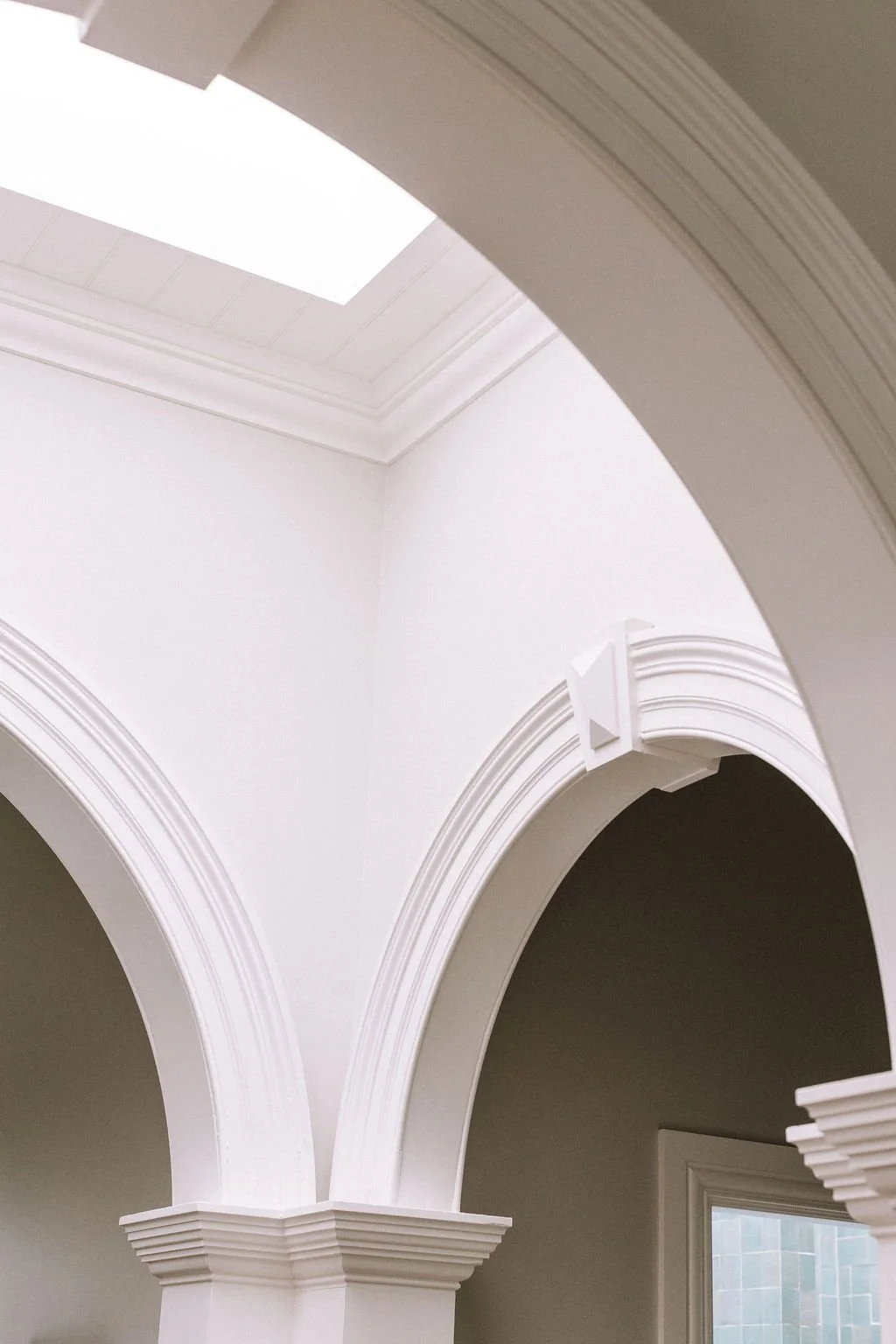 Interior view of a room with white walls, arched doorways, crown molding, and a ceiling with rectangular skylight.