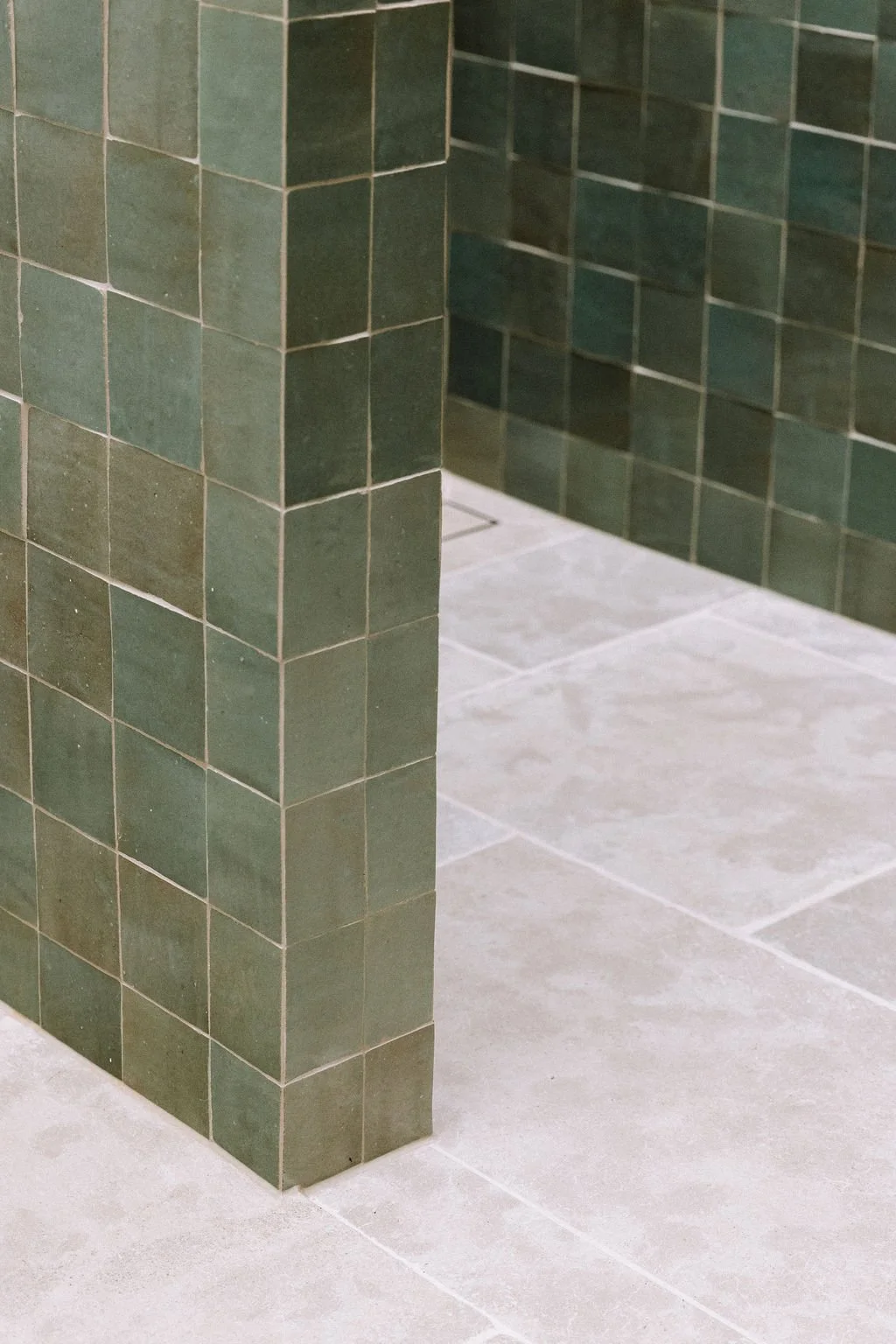 Corner of a shower stall with green tiled walls and beige tiled floor.