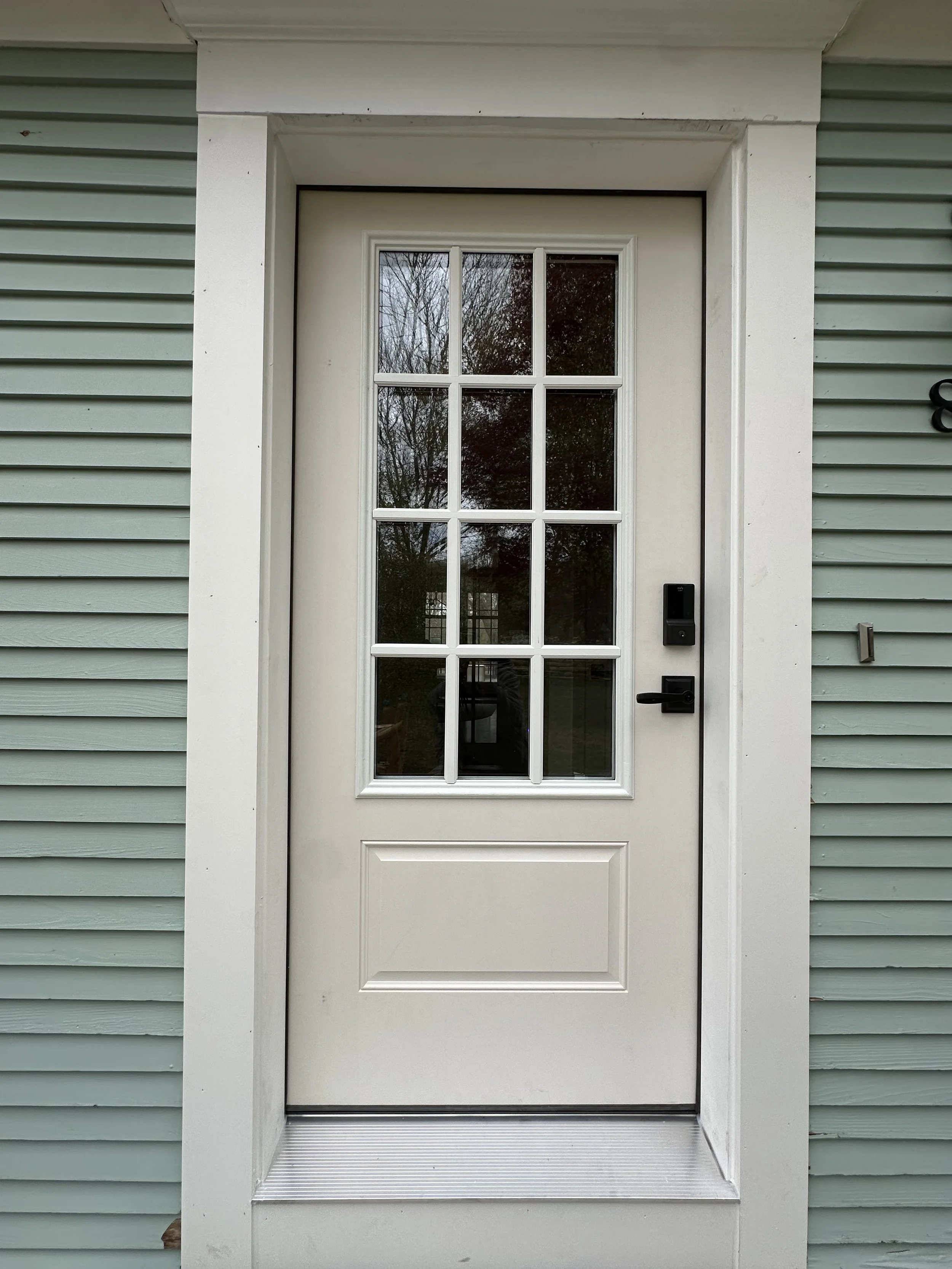 A white door with glass panes and a black electronic lock, set within a white frame, surrounded by teal trim siding.