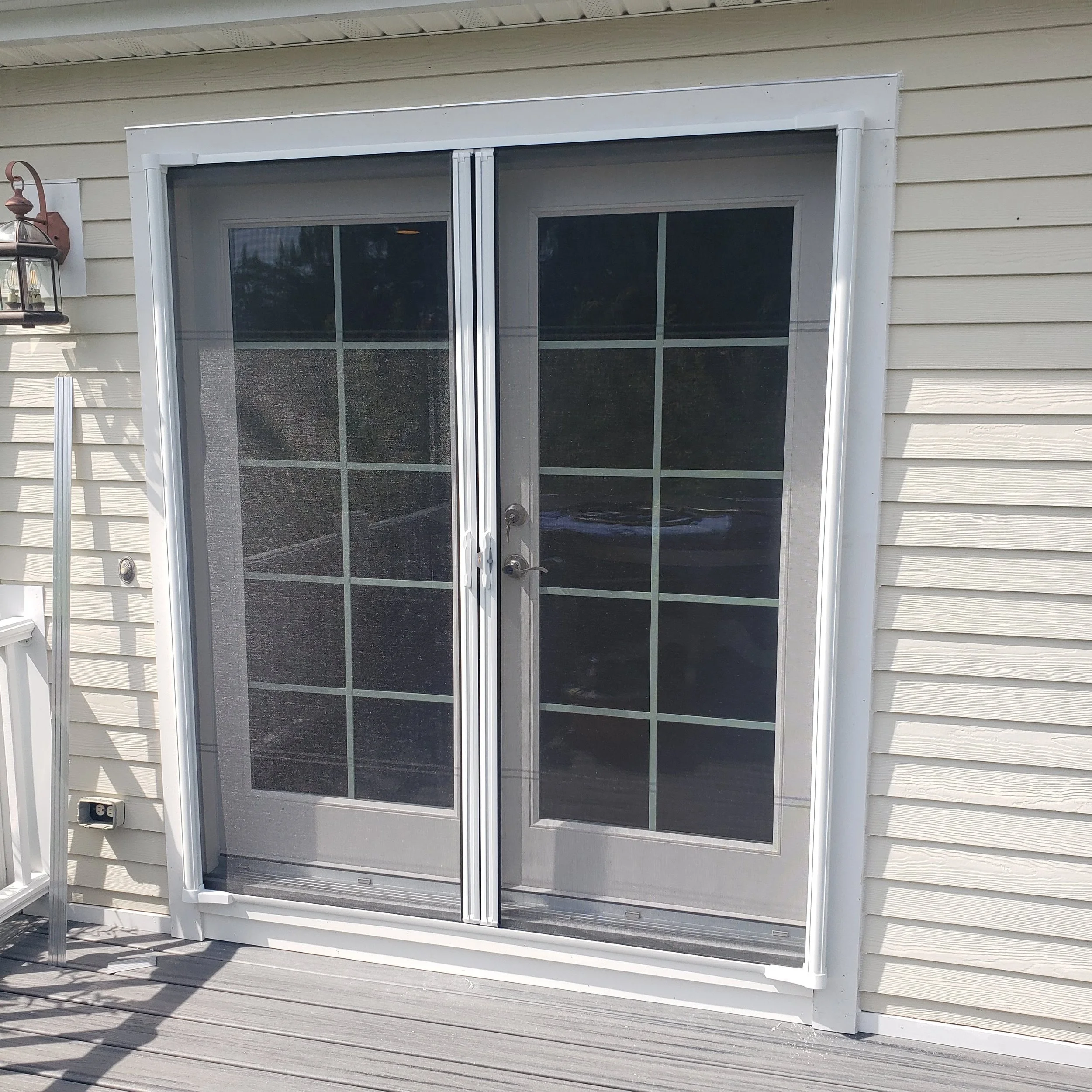 Sliding glass door on a house with beige vinyl siding and outdoor deck, shadow of a railing cast on the deck.