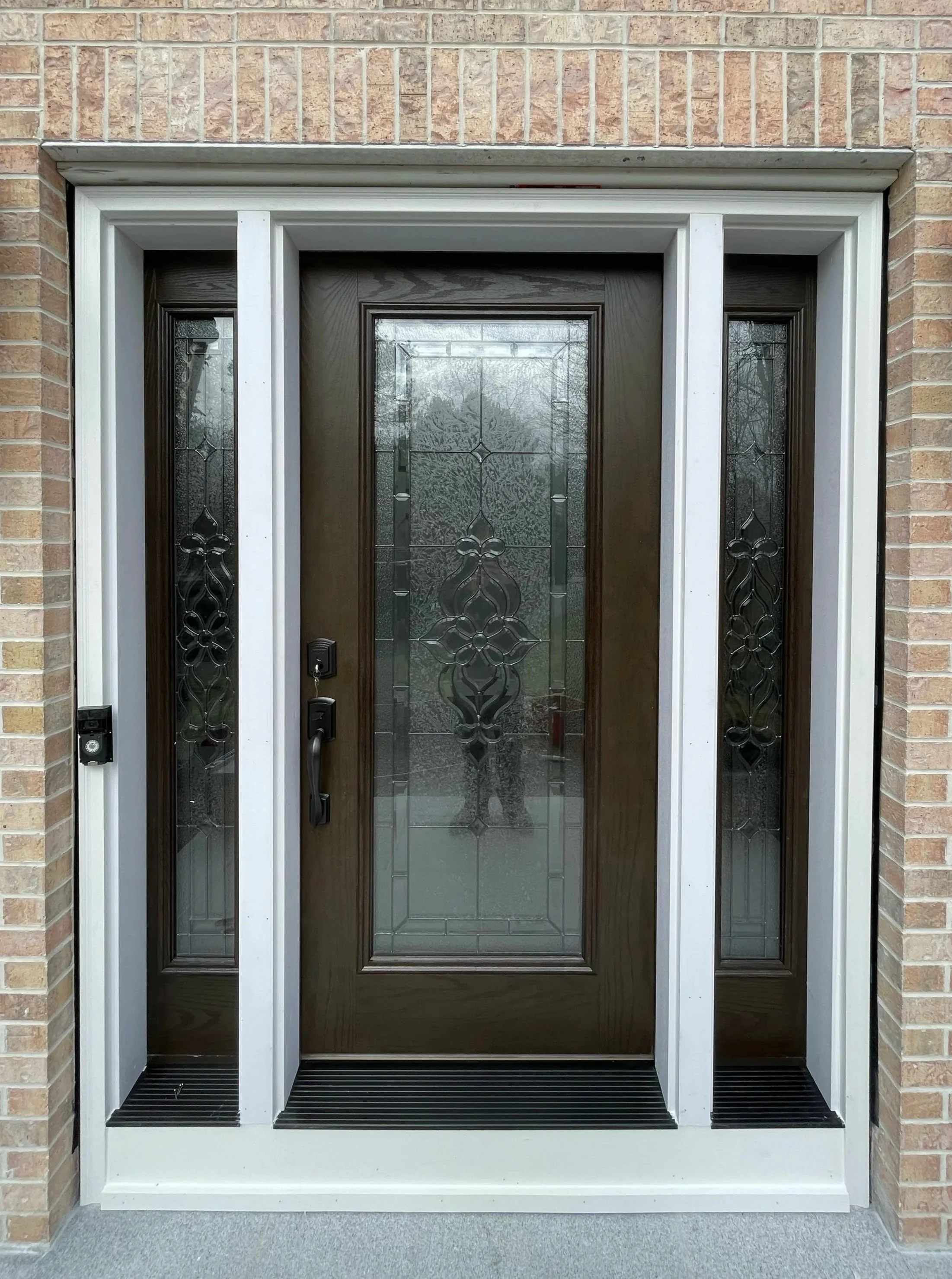Front view of a house's front door with glass and wood design, framed by brick walls and a white door frame.