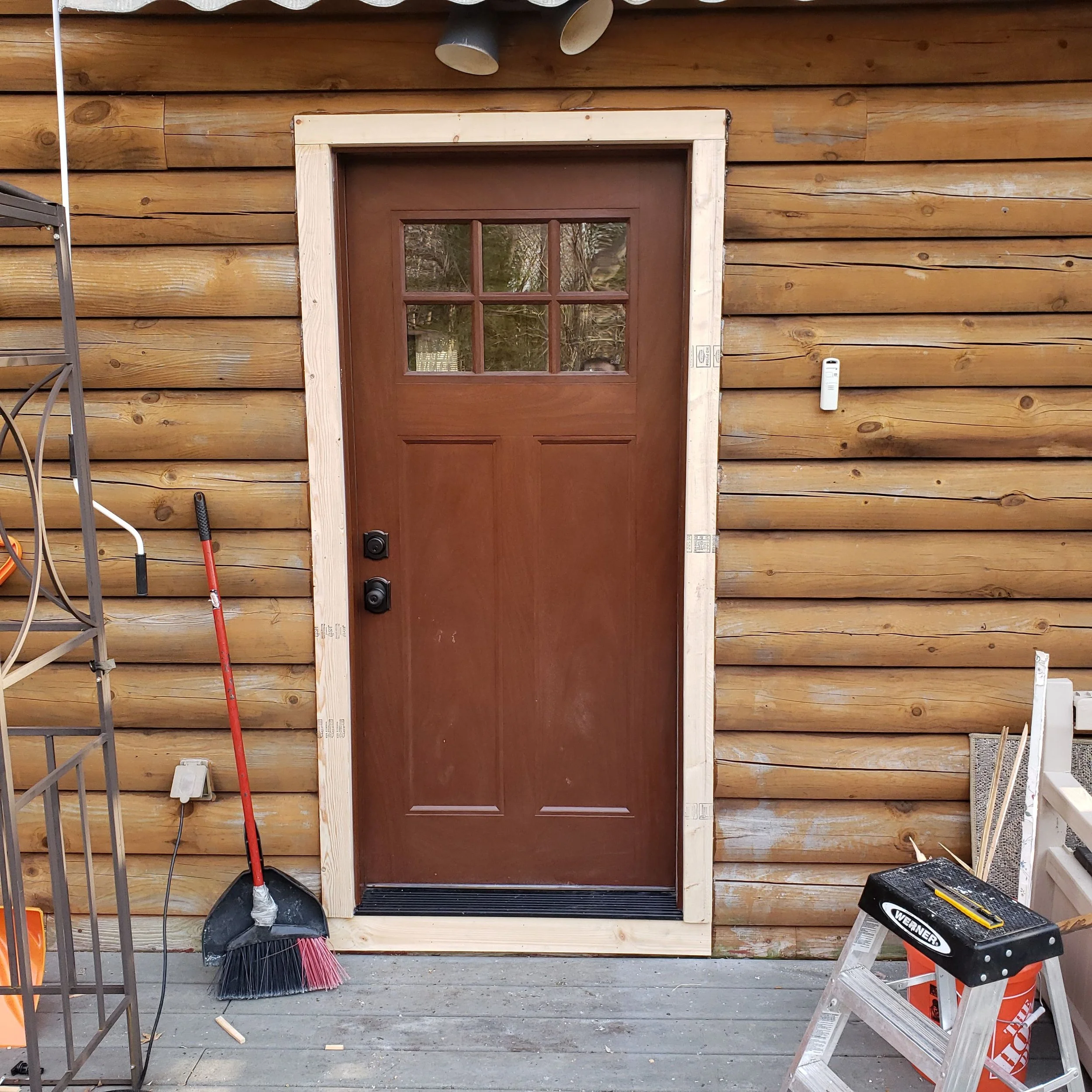 wooden wall with a door under renovation, surrounded by construction tools including brooms, a step ladder, and buckets.
