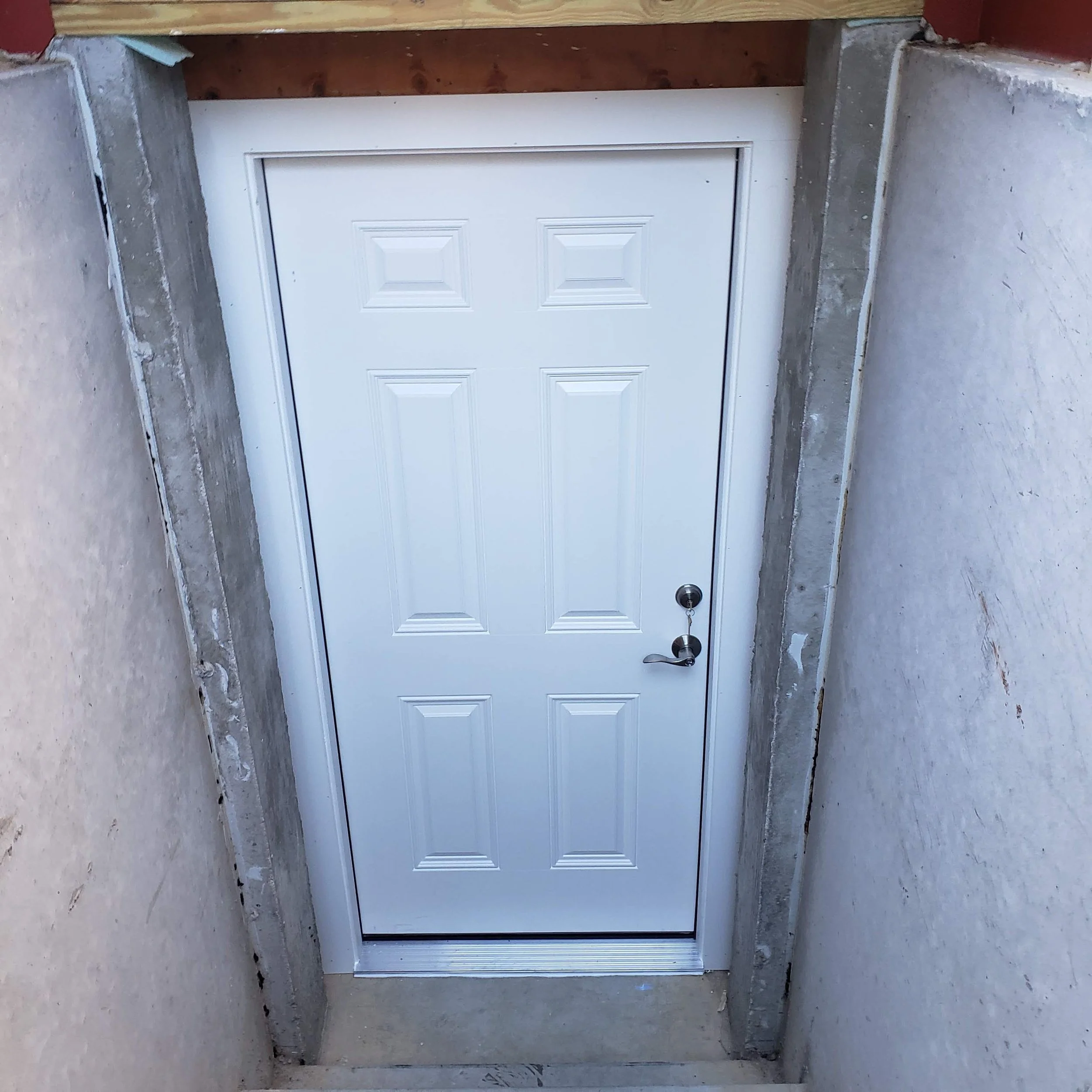 A white paneled door with a silver handle set in a concrete wall, with unfinished construction surrounding it.