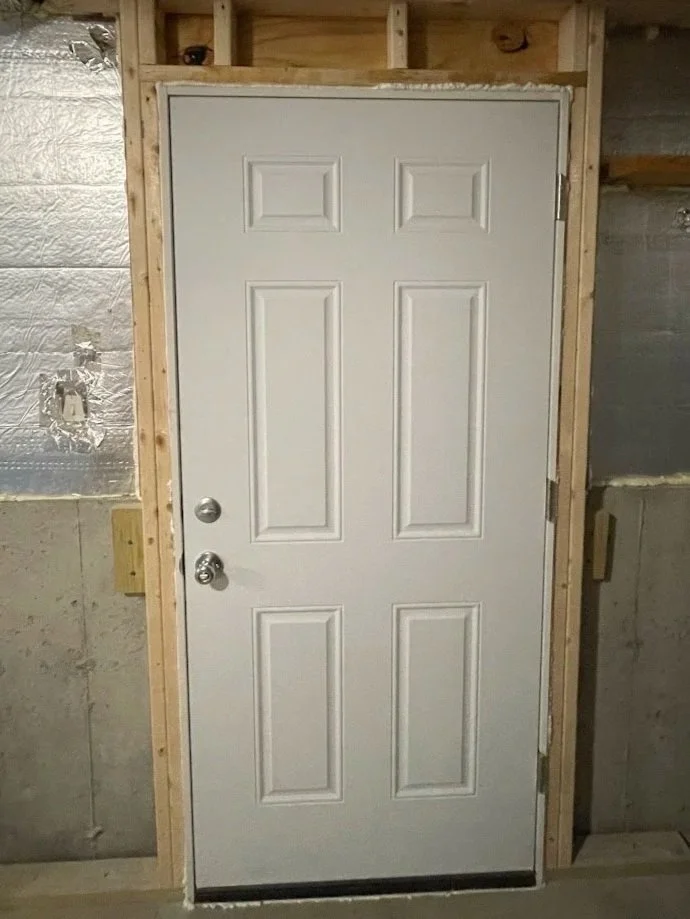 White exterior door with a silver doorknob and a deadbolt, installed in a wooden frame inside a room under construction.