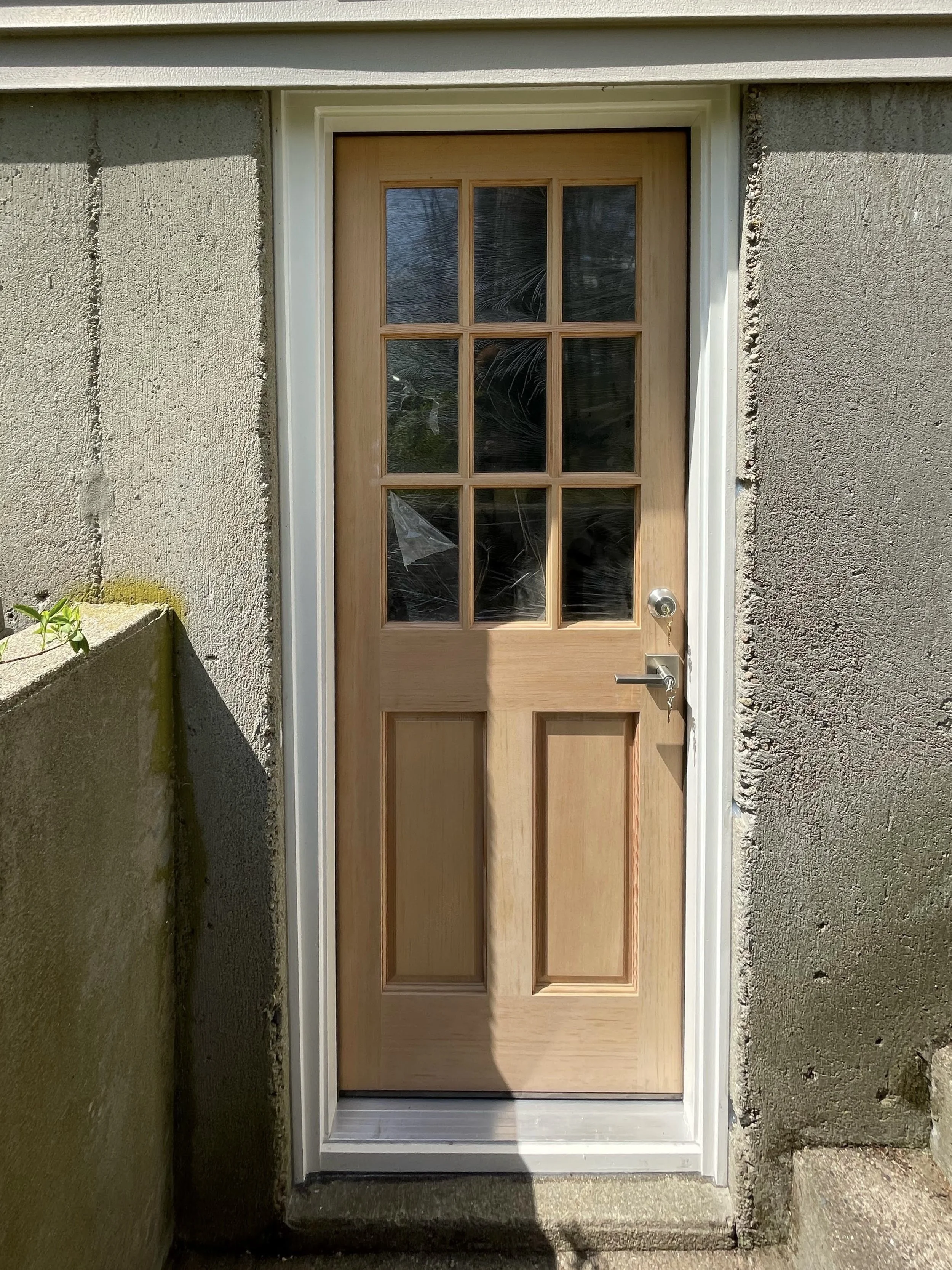 Front view of a wooden door with glass panels set in a gray stucco wall.