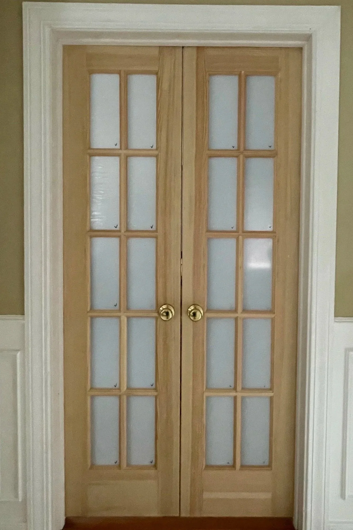 Double glass-paned wooden doors with brass doorknobs, set in a white-framed doorway, leading to another room.