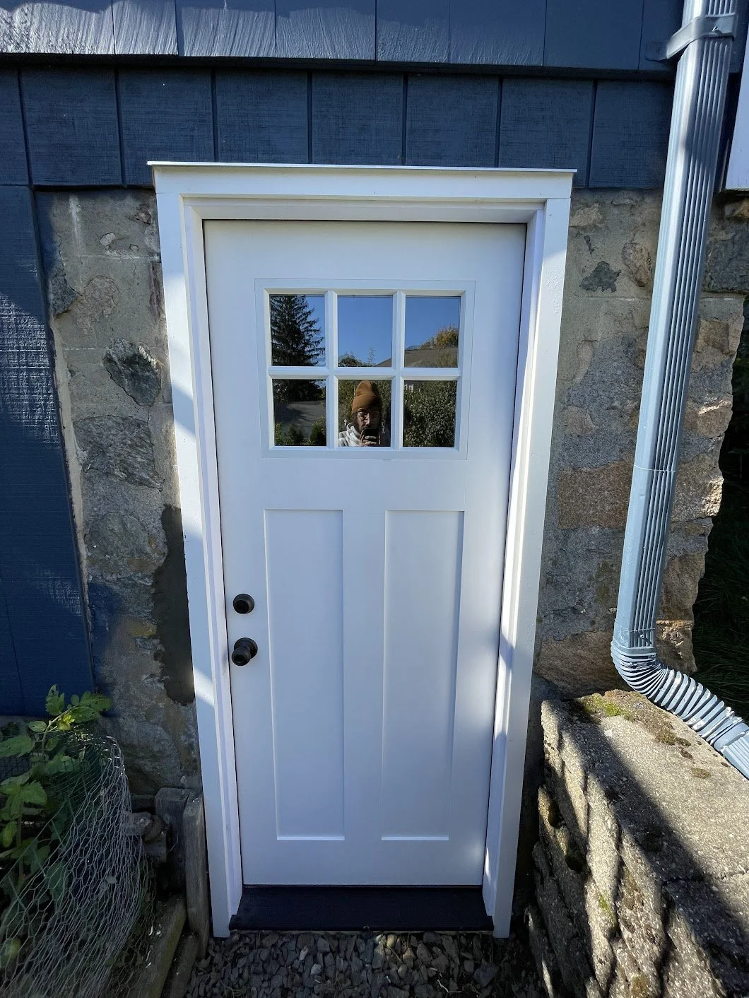 White exterior door with a glass window at the top, set in a stone wall.