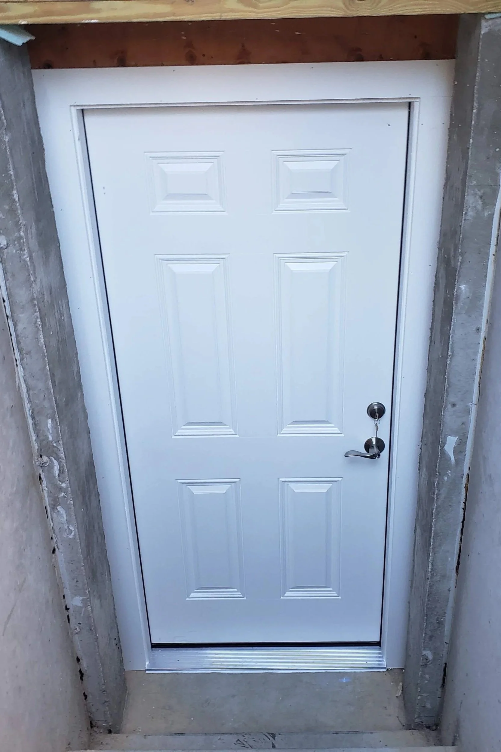 White garage door with six panels, set in a concrete frame with unfinished surrounding walls.