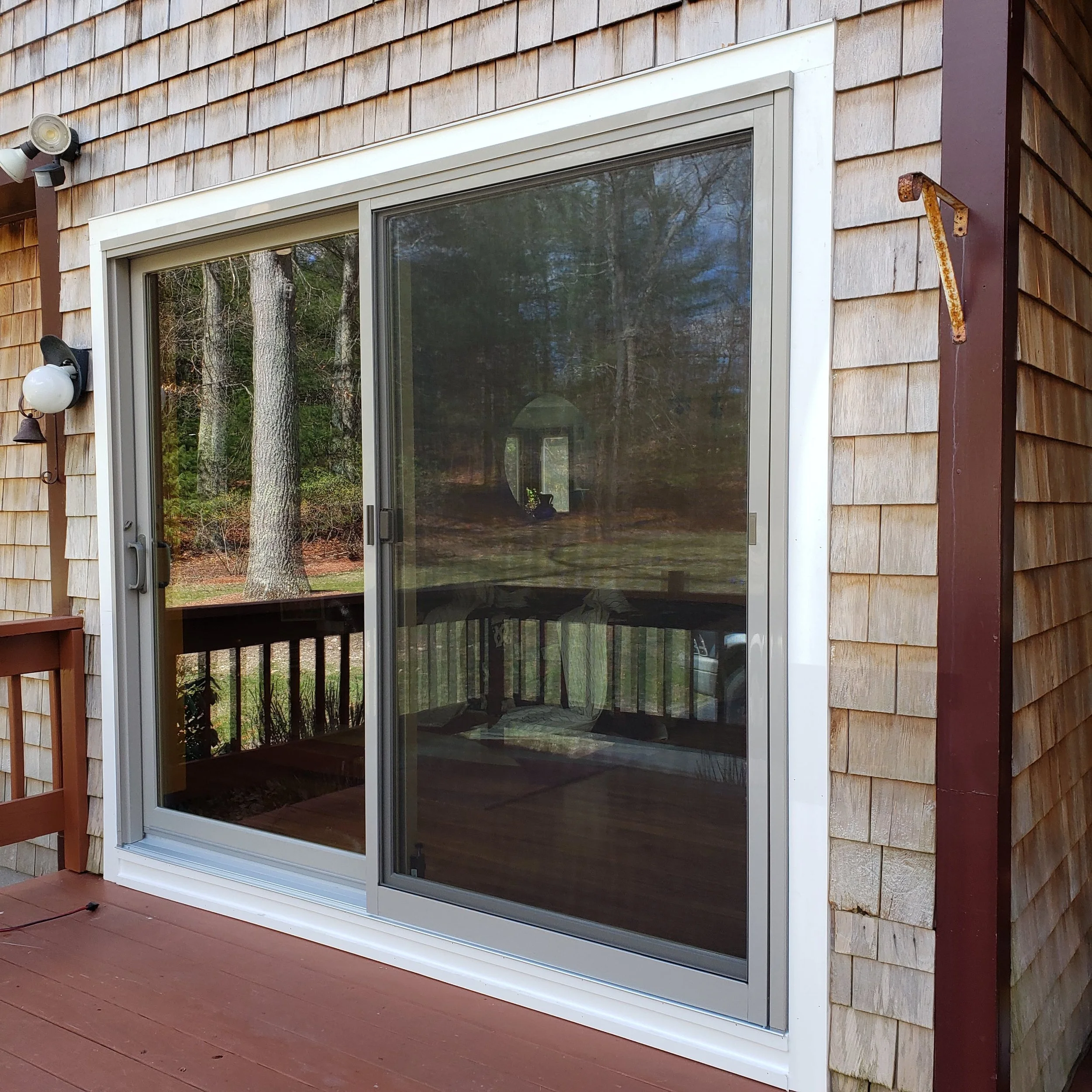 Sliding glass doors on the exterior of a house with shingle siding and a wooden deck in front.