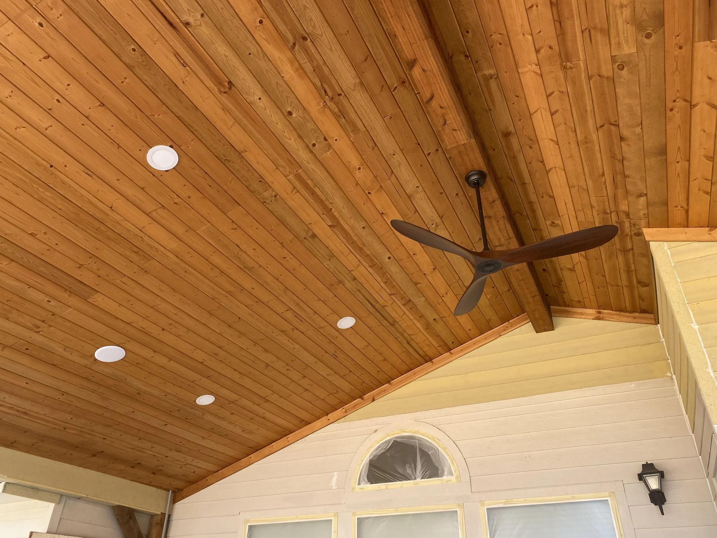 Ceiling with wood planks, recessed lights, ceiling fan, and a small portion of the wall with a window and light fixtures.