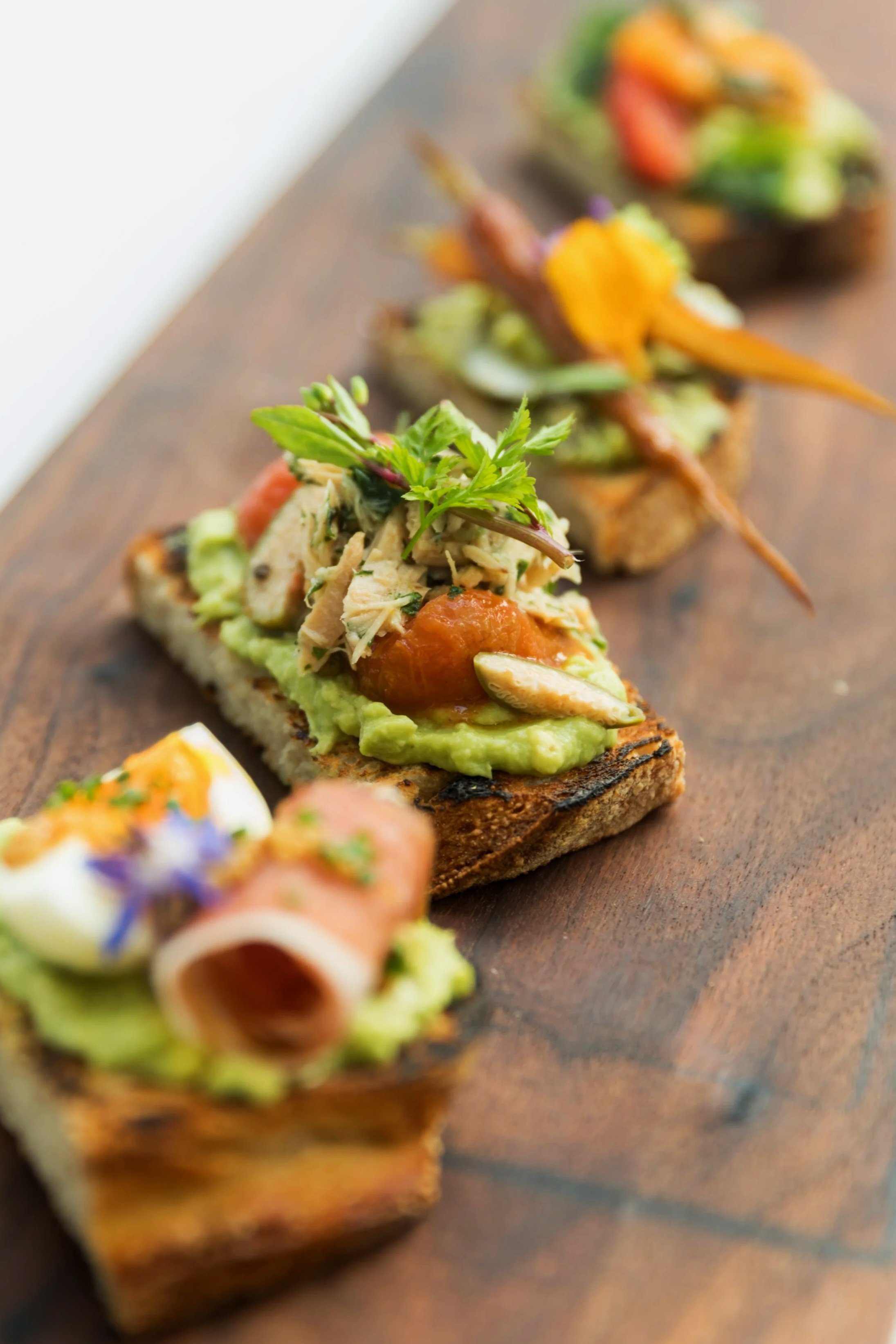 Close-up of colorful gourmet appetizers on a wooden serving board, featuring various toppings and garnishes.
