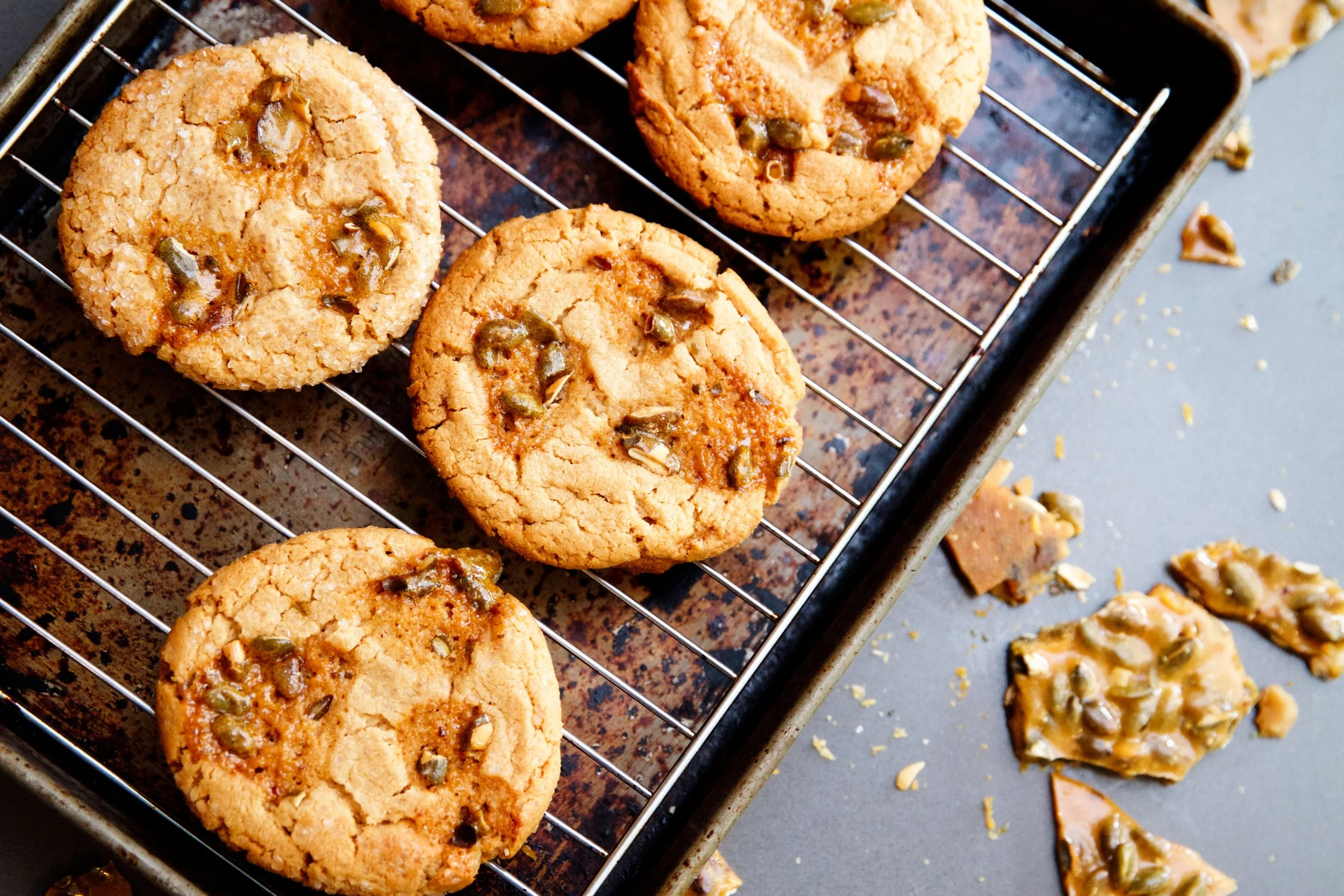Close-up of seven chocolate chip cookies with some sprinkled with chopped nuts on a wire cooling rack over a baking sheet.