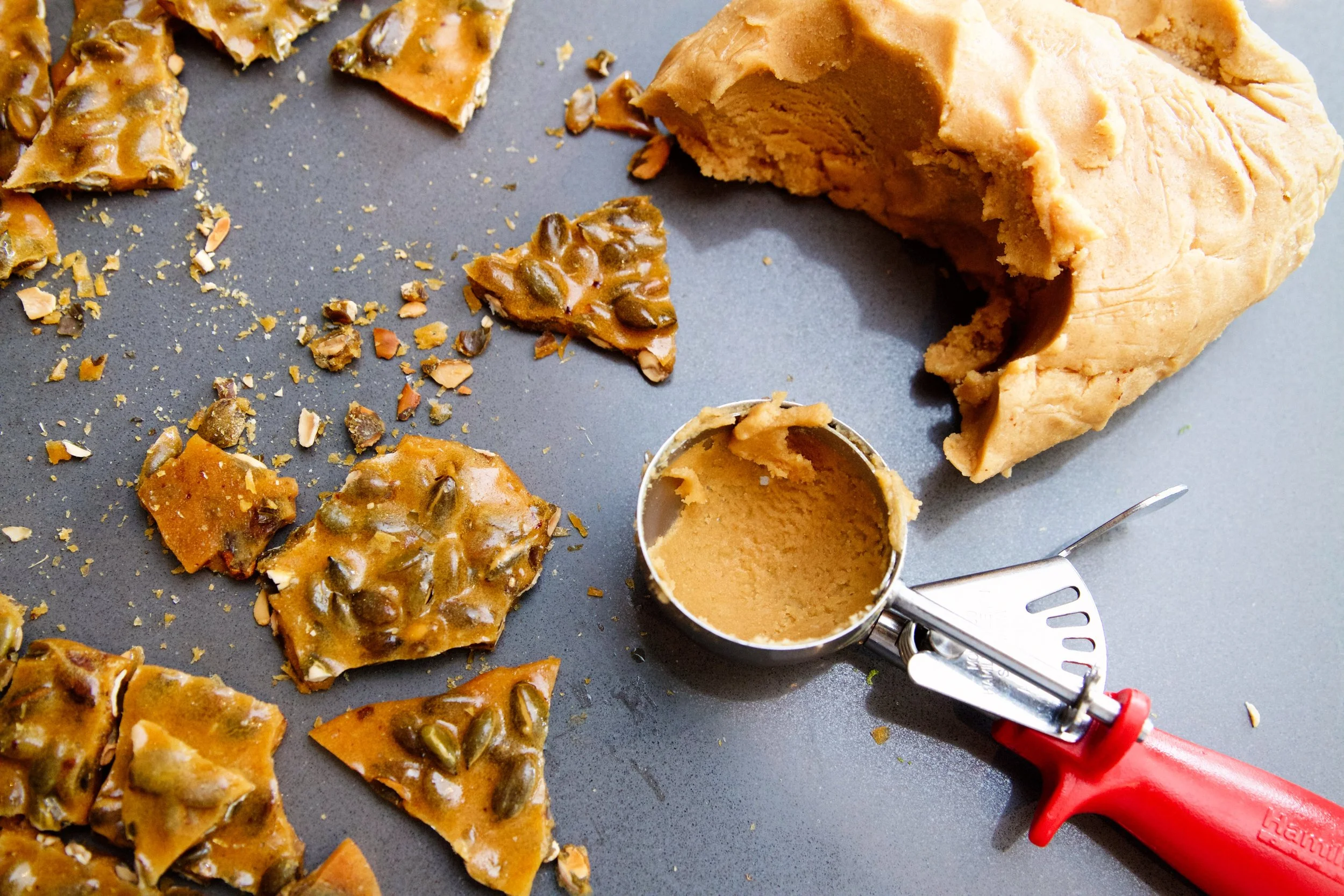 Fudge with a piece removed showing its creamy interior, surrounded by broken pieces and a metal spatula on a dark surface.