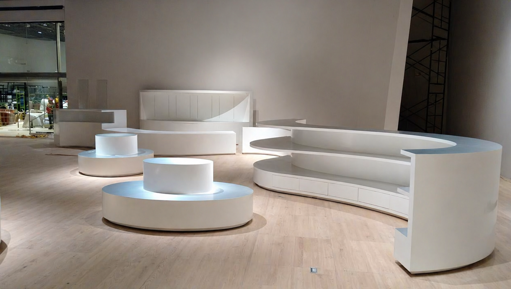 Mueble blanco moderno y curvado en una exhibición interior con piso de madera clara y pared gris, en un espacio que parece una tienda o galería.