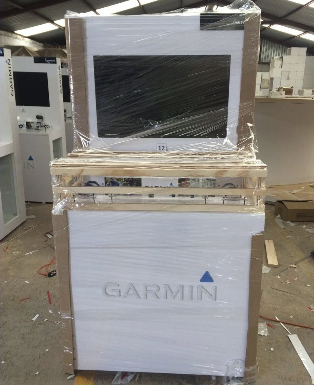 Caja de embalaje para un televisor Garmin, todavía envuelta en plástico, en una tienda o almacén.