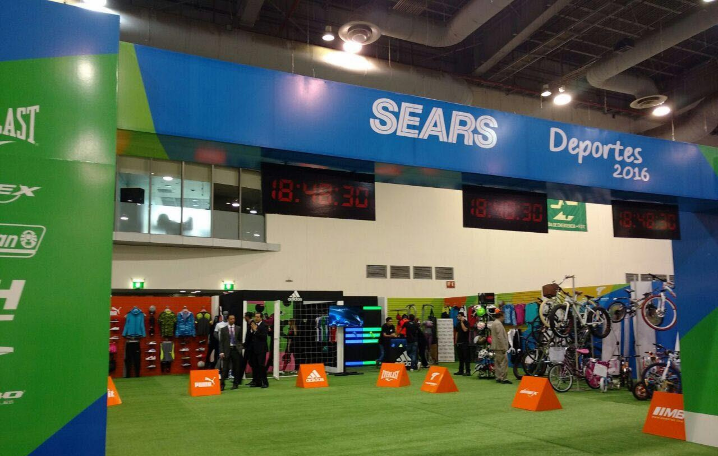 Interior de una tienda deportiva llamada Sears con artículos como bicicletas, ropa y equipos deportivos, y un letrero que dice 'Deportes 2016'.