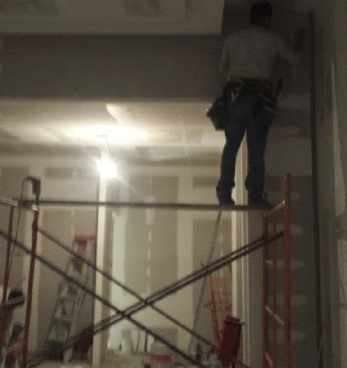 Persona en una plataforma de construcción en un interior con escaleras y andamios, algunas de ellas en zigzag. La persona lleva una mochila y parece estar en una zona en proceso de reparación o construcción.