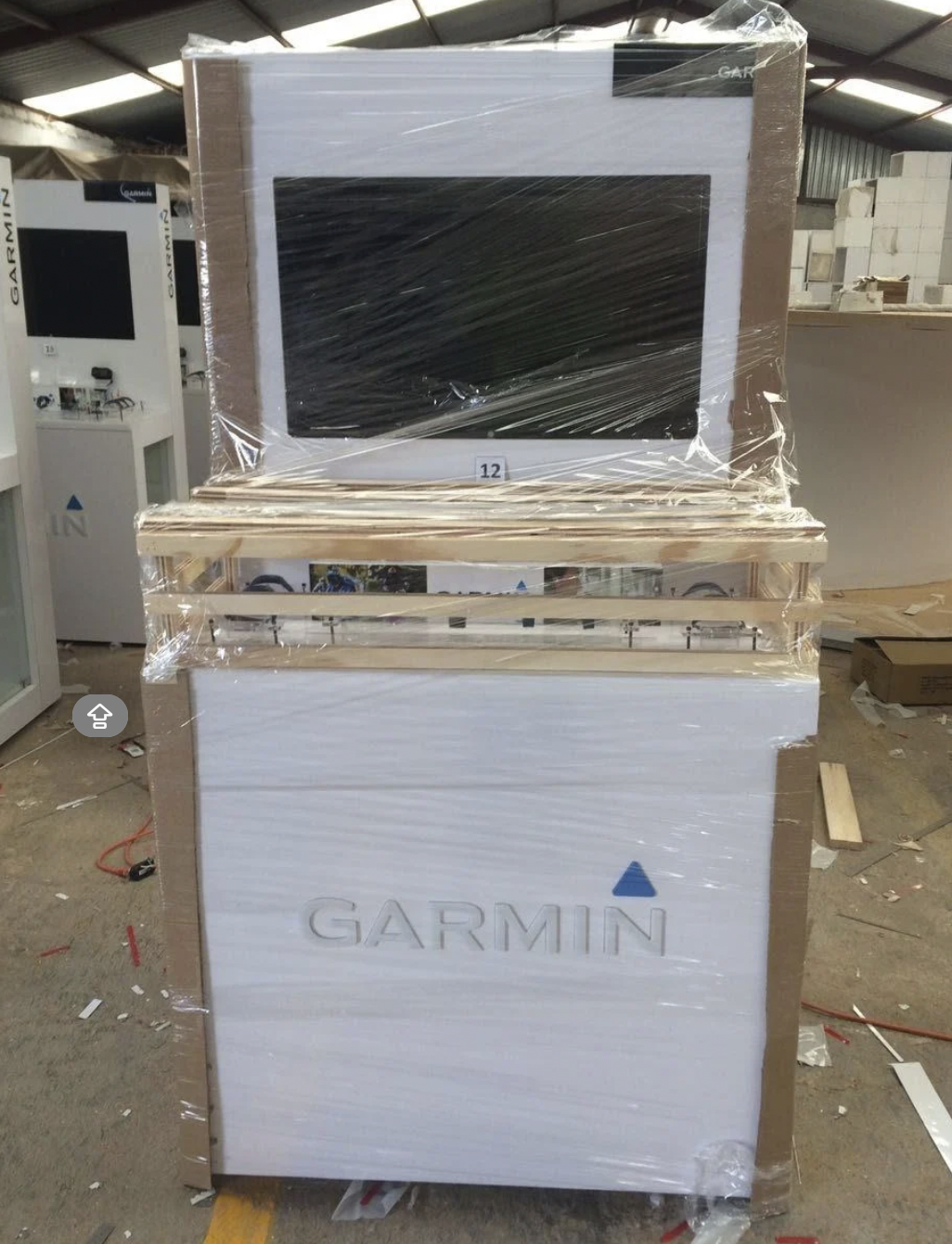 Caja de embalaje con pantalla Garmin y otros componentes electrónicos, envuelta en plástico y ubicada en un almacén