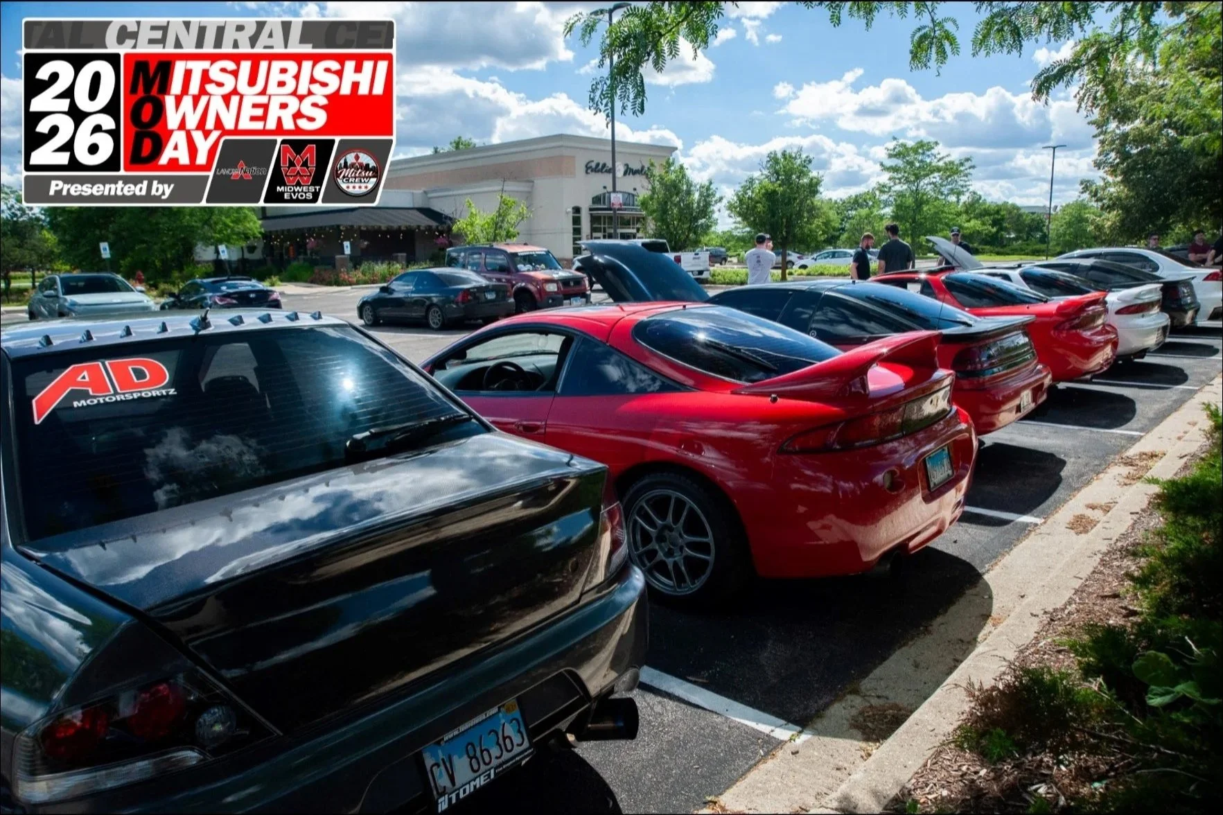 Multiple sports cars parked in a parking lot with a shopping center in the background, under a partly cloudy sky.