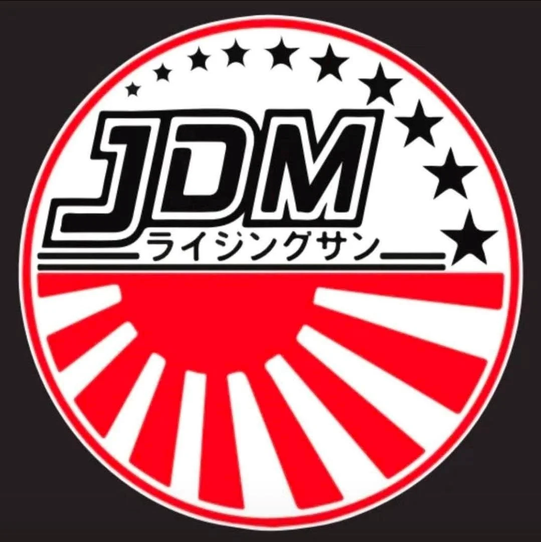 A circular logo with black, white, and red colors featuring the text 'JDM' in bold black font, Japanese characters, and a design of a sunrise with rays, stars, and a red sun in the background.