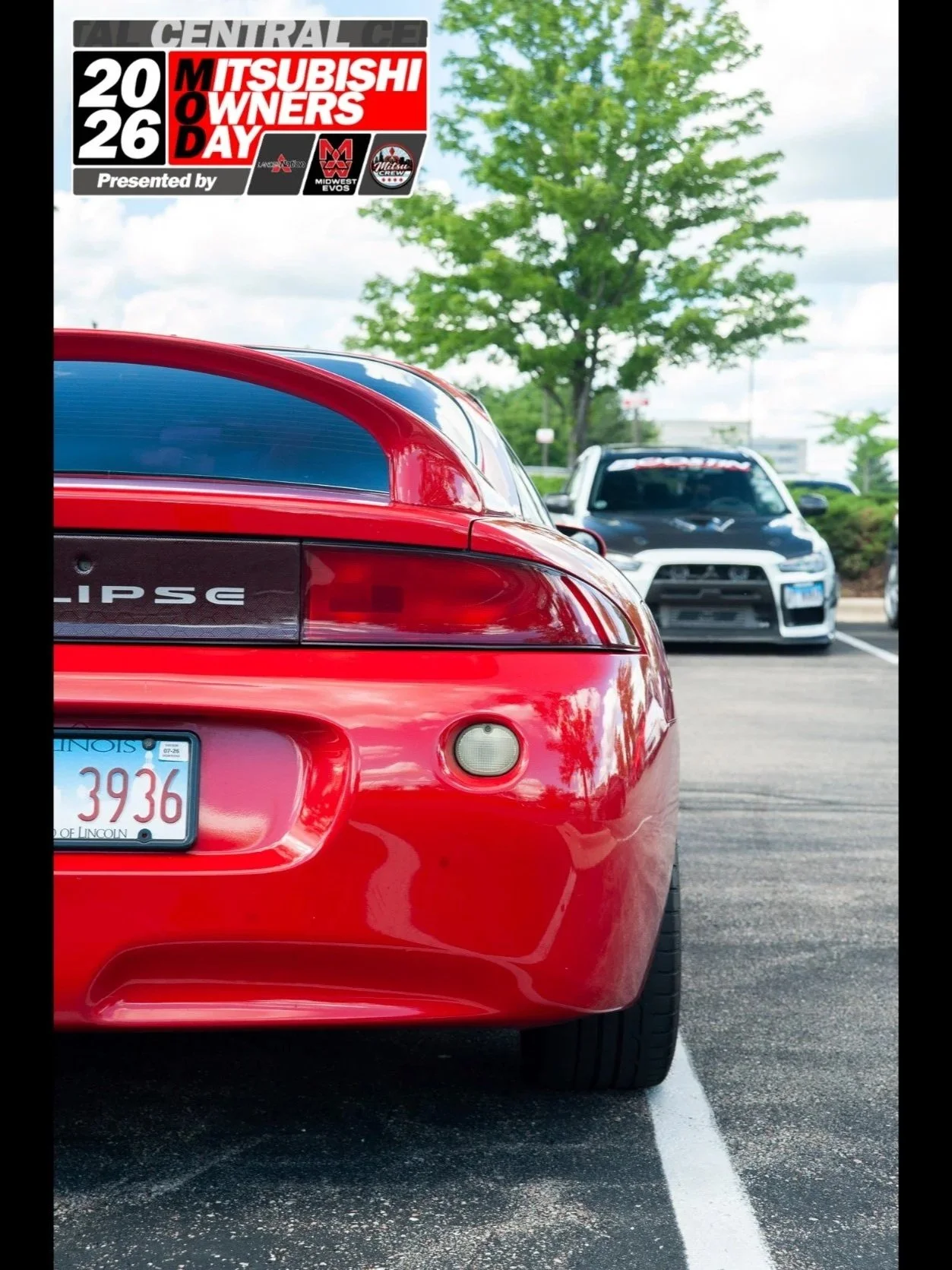 The rear view of a red Mitsubishi Eclipse sports car parked in a parking lot, with a black and white car and a tree with green leaves in the background. There is a sign on the upper left corner promoting Mitsubishi Owners Day 2026.