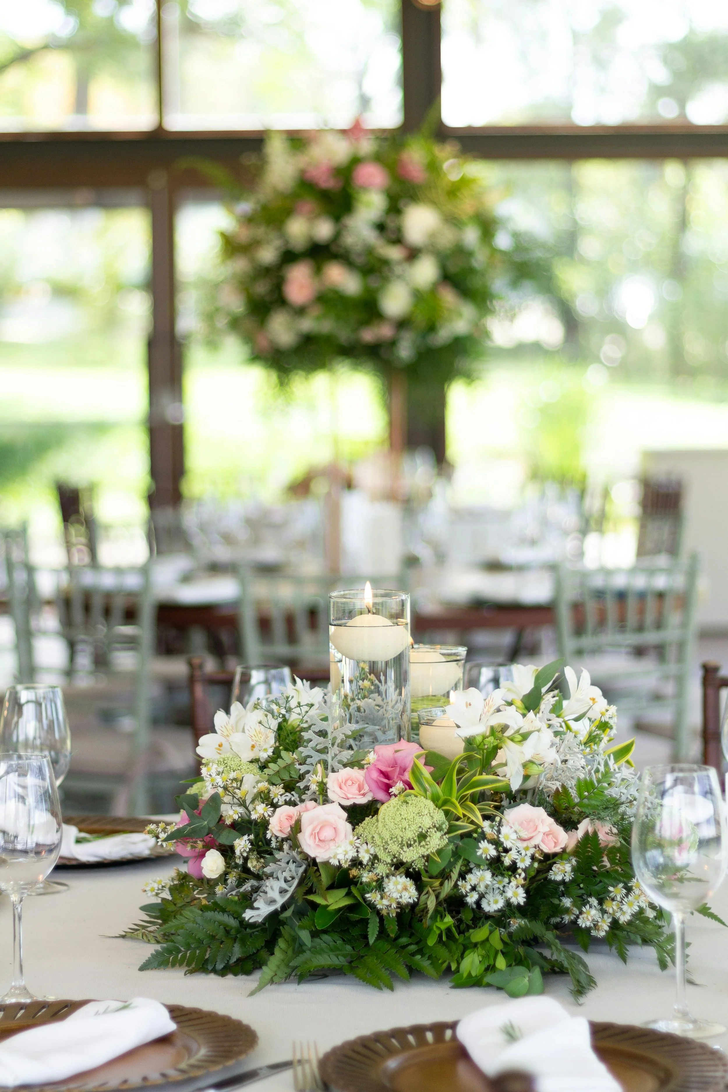 Elegant dining table with a lush floral centerpiece, surrounded by wine glasses and place settings, in a bright room with large windows overlooking greenery.