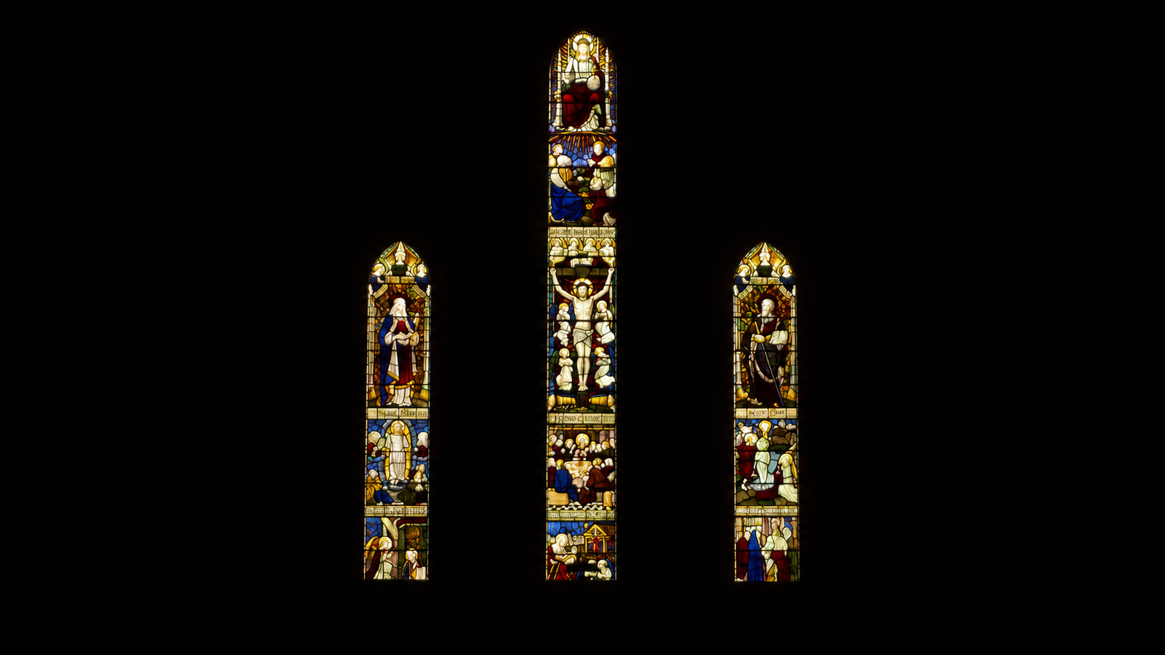 Colorful stained glass windows depicting religious scenes, with a central window featuring Jesus Christ on the cross, illuminated against a dark background.