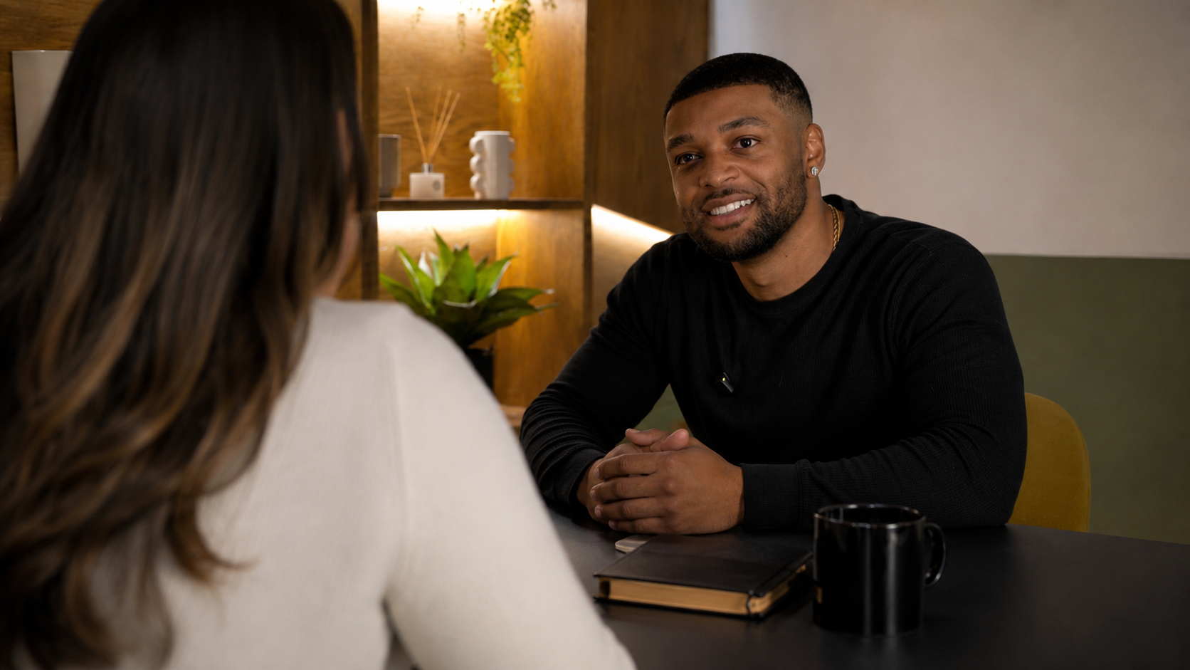 Stefan Saunders talking to a woman during a meeting, with a notebook and laptop on the table.