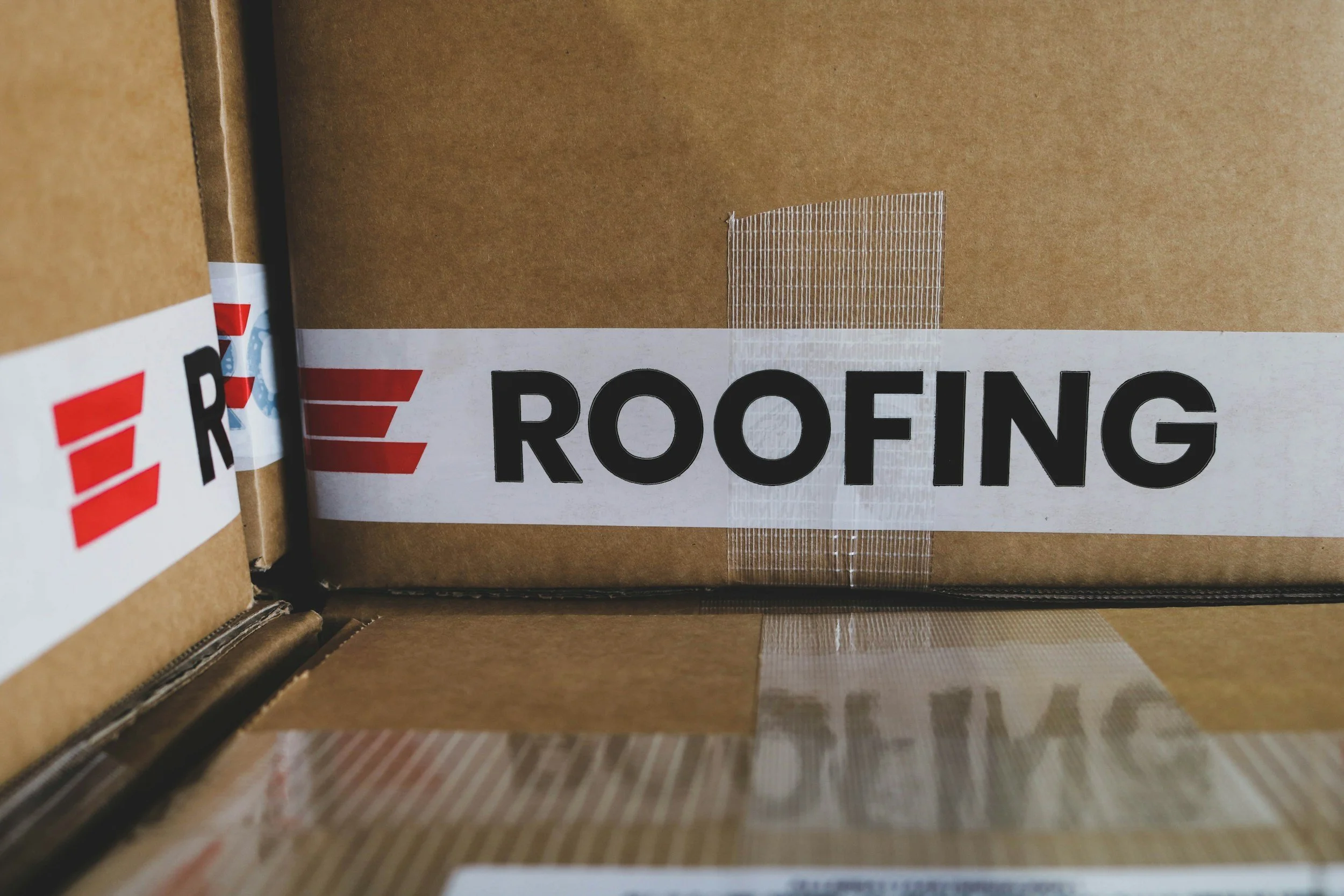 Stacked cardboard boxes with a label that says "ROOFING" on the front.
