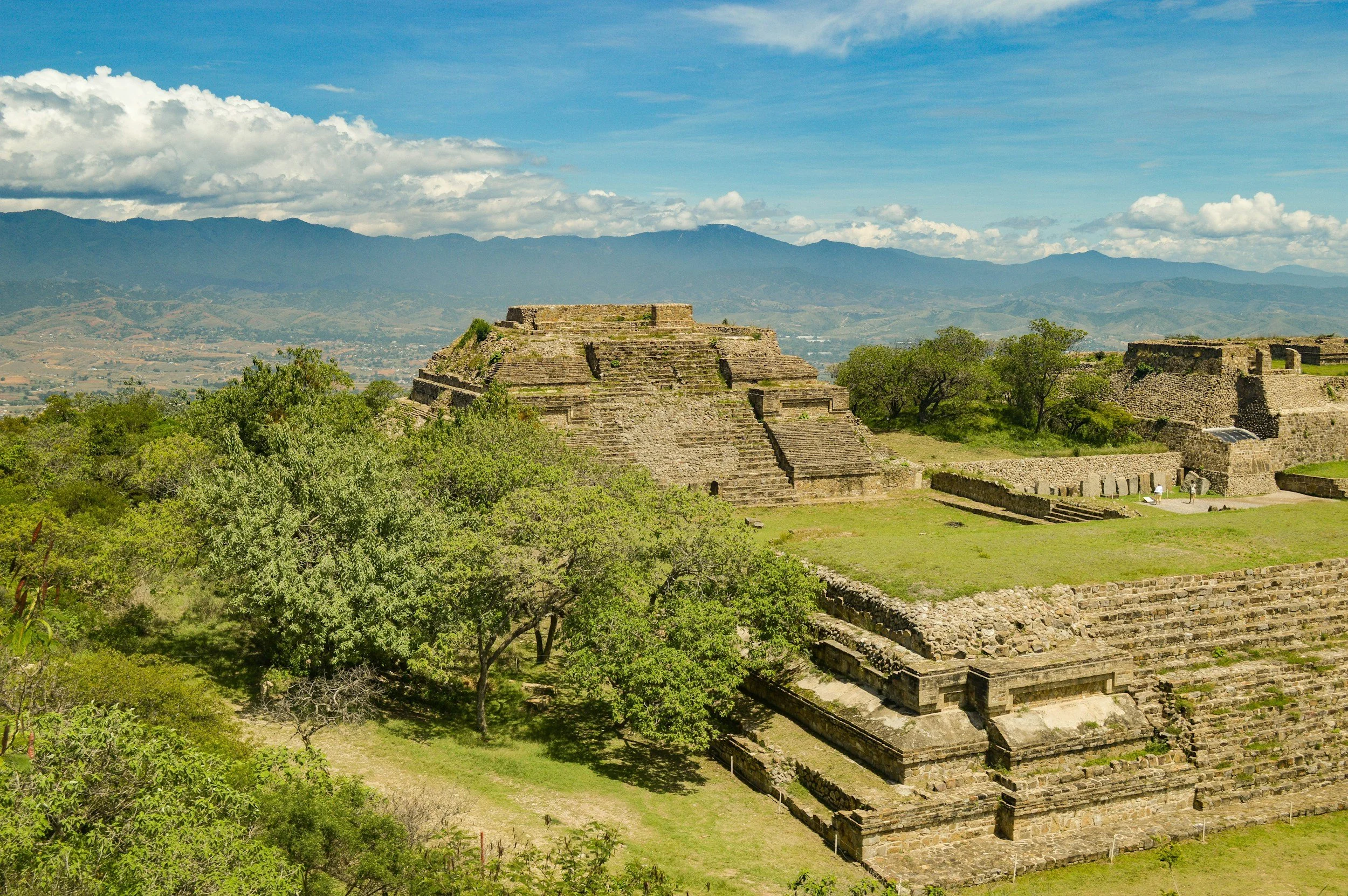 Pirámide antigua en la zona arqueológica de Palenque, rodeada de vegetación y montañas al fondo bajo un cielo con nubes.