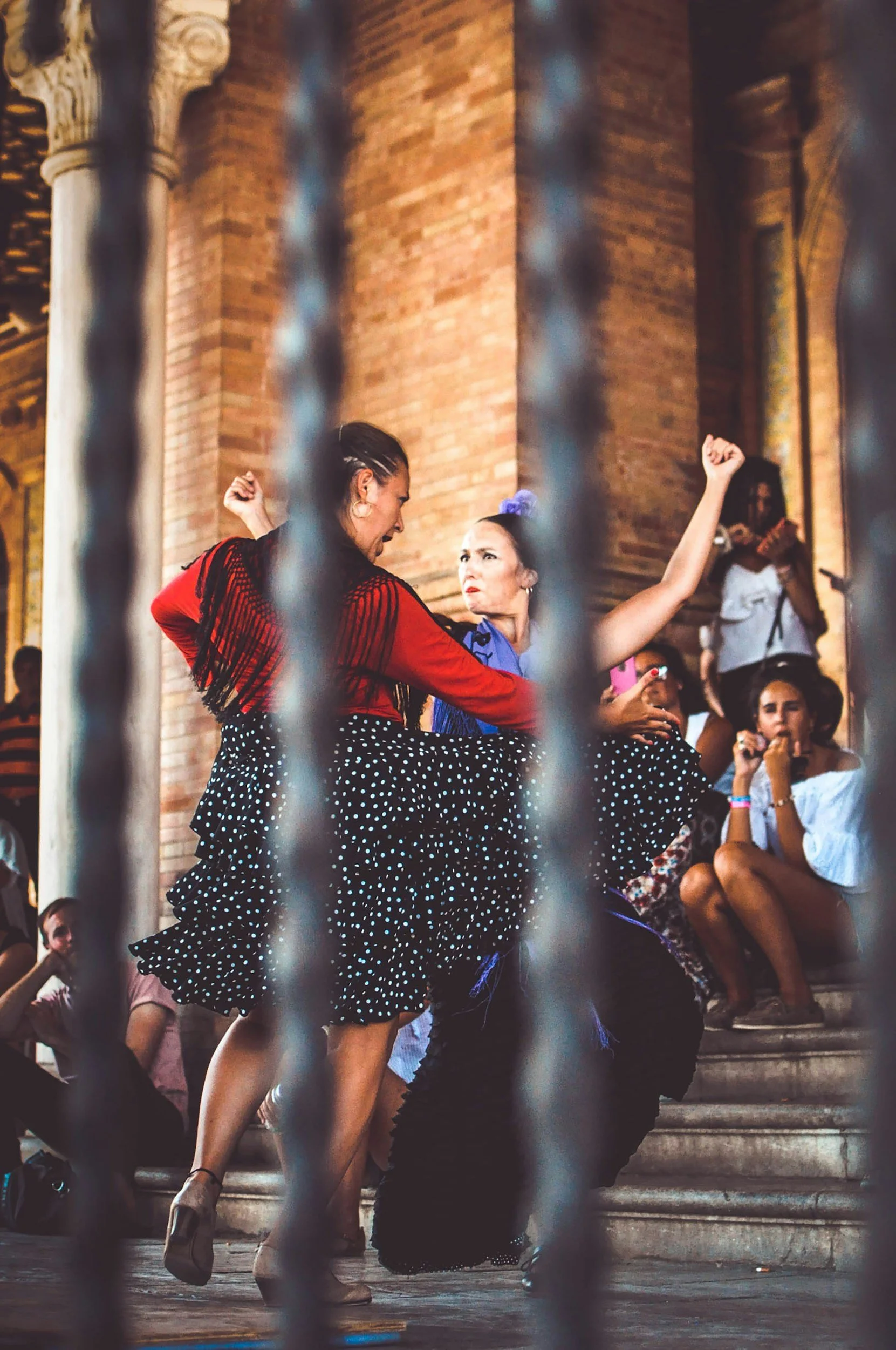 Dos mujeres bailando flamenco frente a una audiencia en una iglesia de ladrillo, vista a través de unas rejas metálicas.
