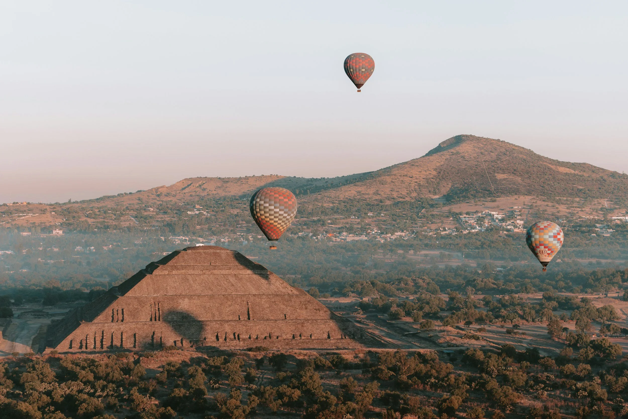 Tres globos aerostáticos sobre una zona montañosa y un templo con techo cónico en primer plano.