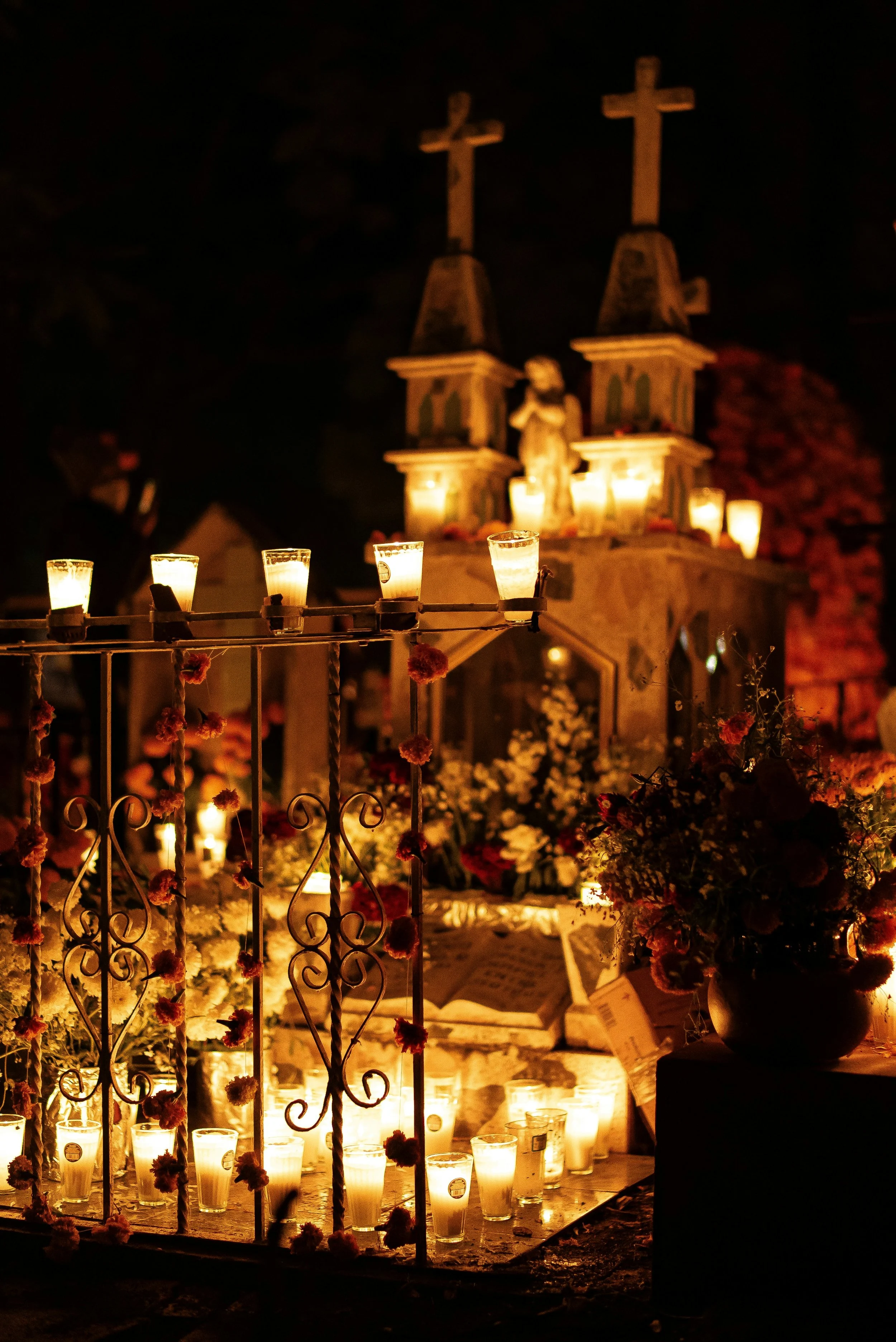 Velas encendidas y flores adornando una estructura de hierro con cruces en una ceremonia nocturna religiosa.