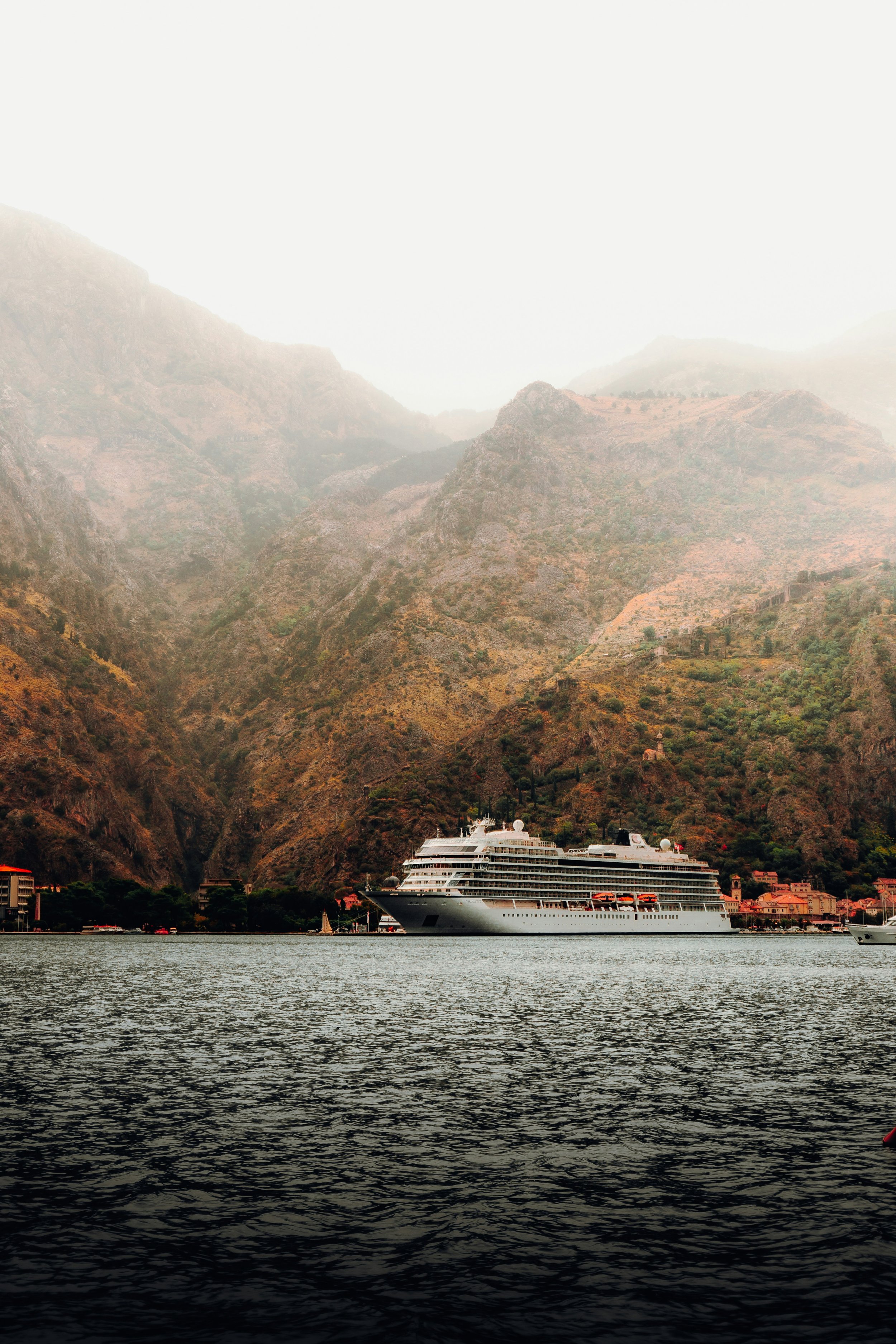 Crucero grande navegando por el rio Nilo con montañas en el fondo cubiertas de vegetación y niebla en la parte superior.