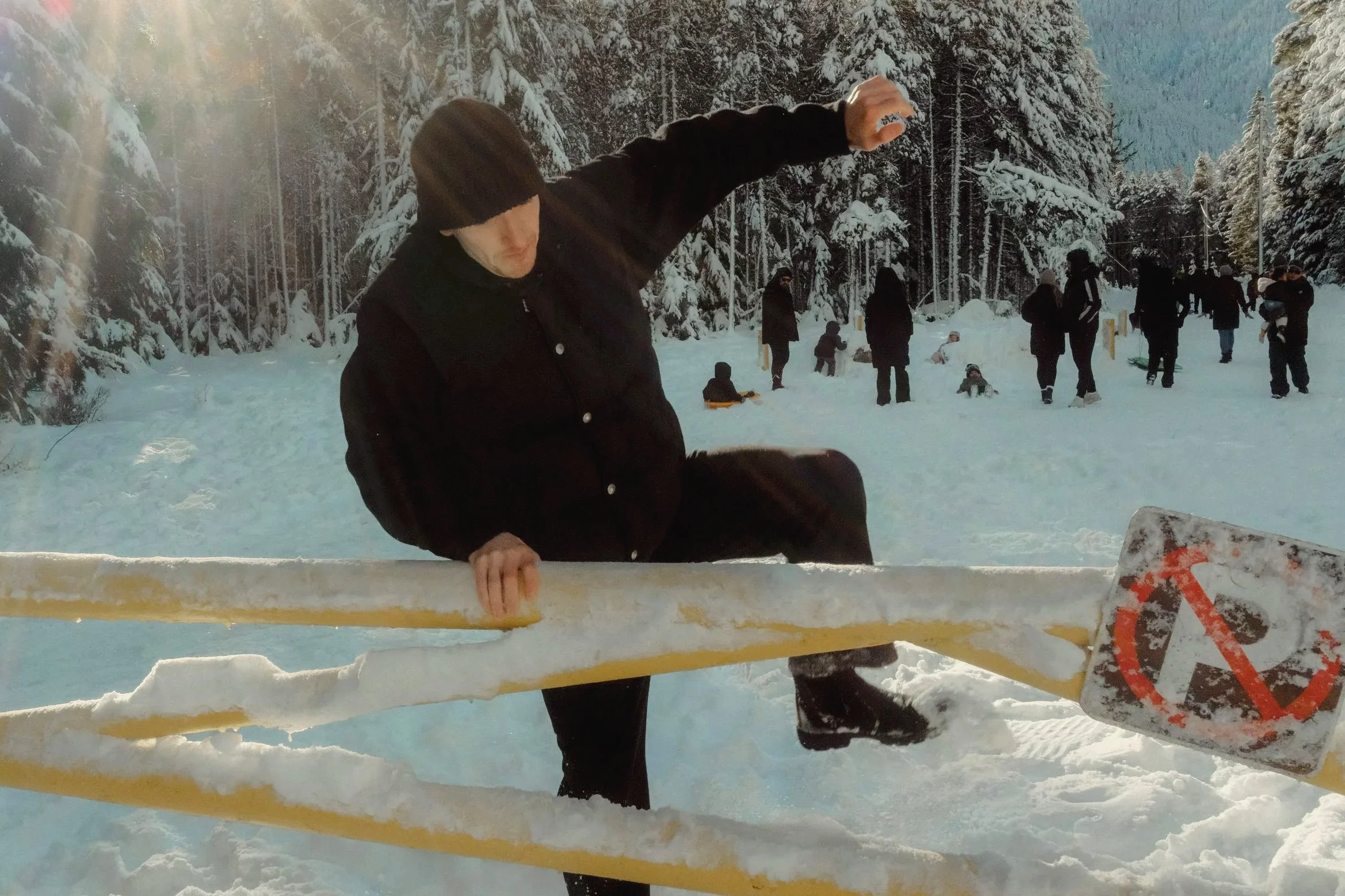 Persona en el hielo con un esquí en la mano y una máscara facial, en un paisaje nevado con árboles cubiertos de nieve y otros niños y adultos en el fondo.