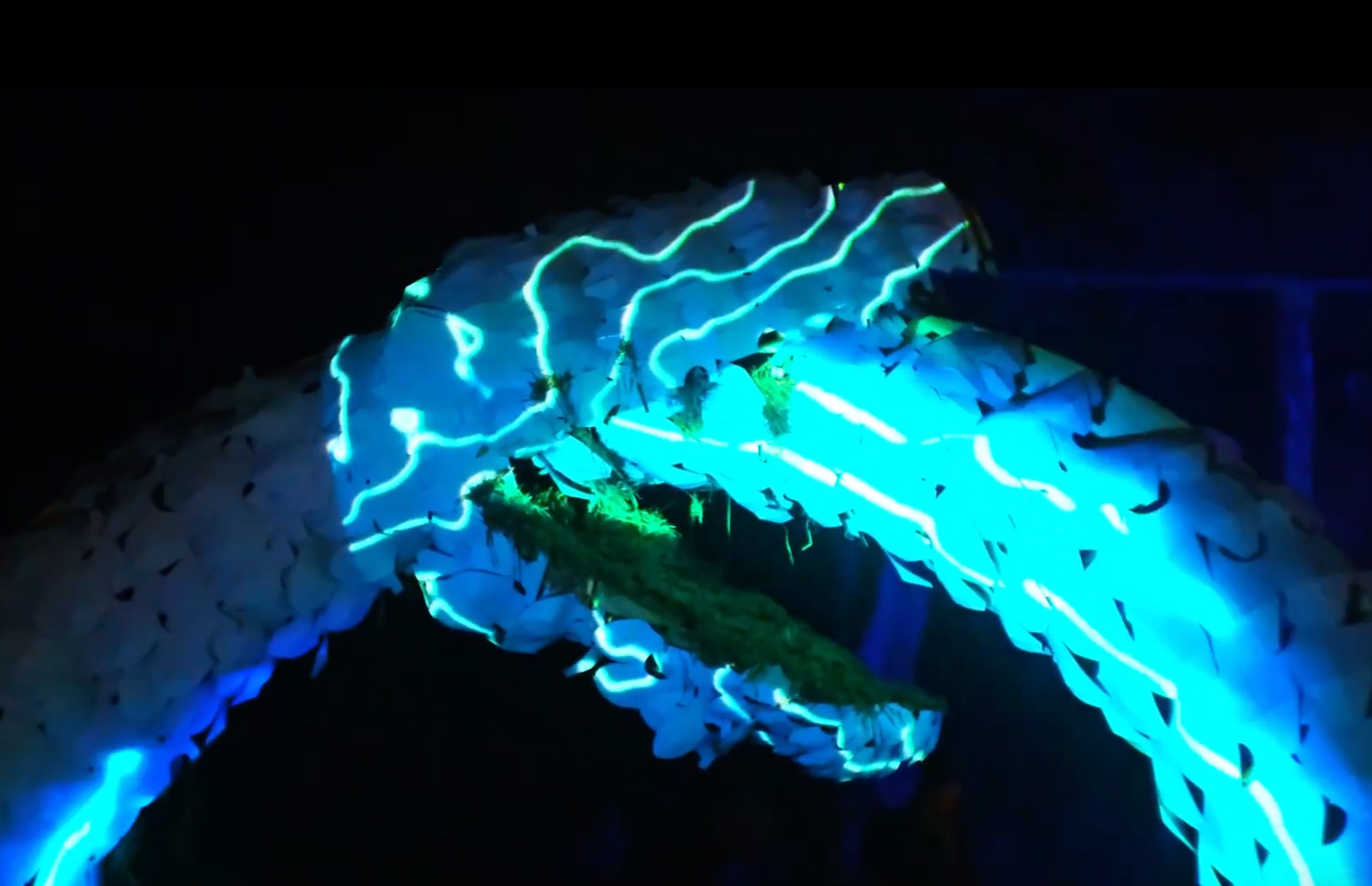 Illuminated sculpture with glowing blue and green light patterns at night.