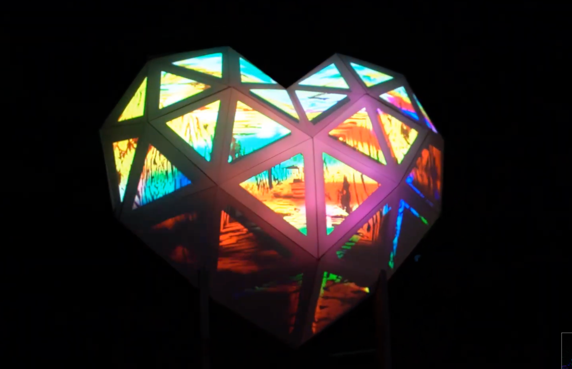 Colorful geometric 3D diamond-shaped sculpture emitting vibrant light reflections, set against a dark background.