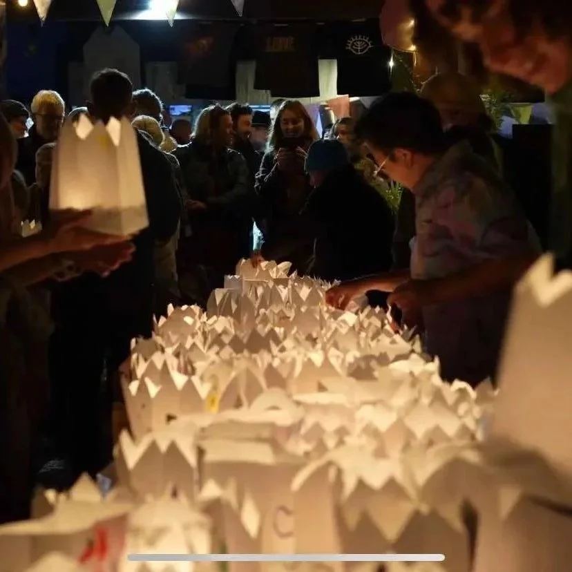 People gathered around a table with illuminated paper lanterns, possibly at a nighttime event or celebration.