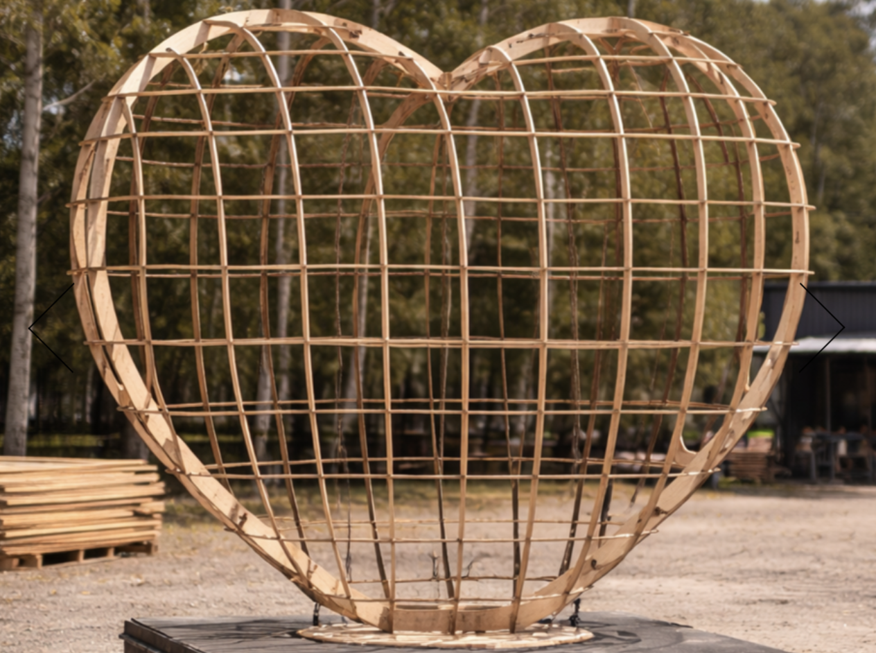 A large wooden heart-shaped sculpture under construction outdoors with a grid of intersecting wooden slats.