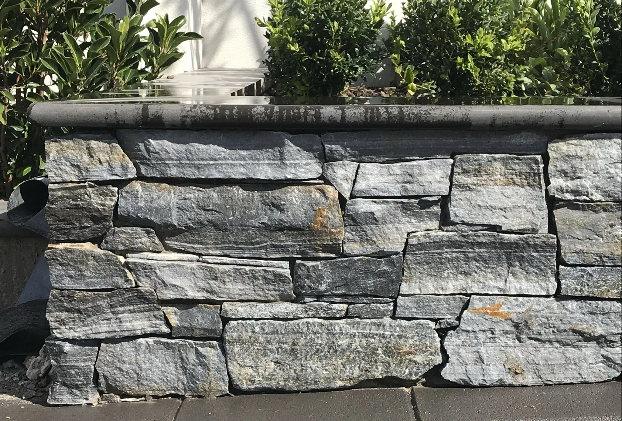 Close-up of a stone garden wall with greenery in the background.