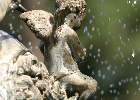 Close-up of a weathered stone statue of a cherub or angel with water splashing around it.
