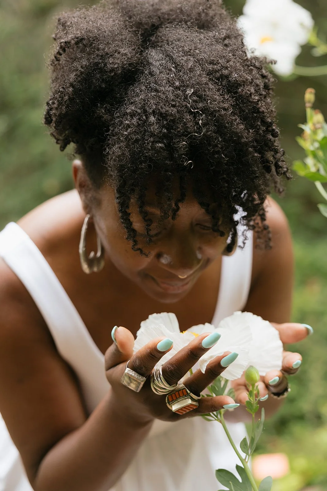 A woman with curly hair looking down and smiling while holding white flowers.