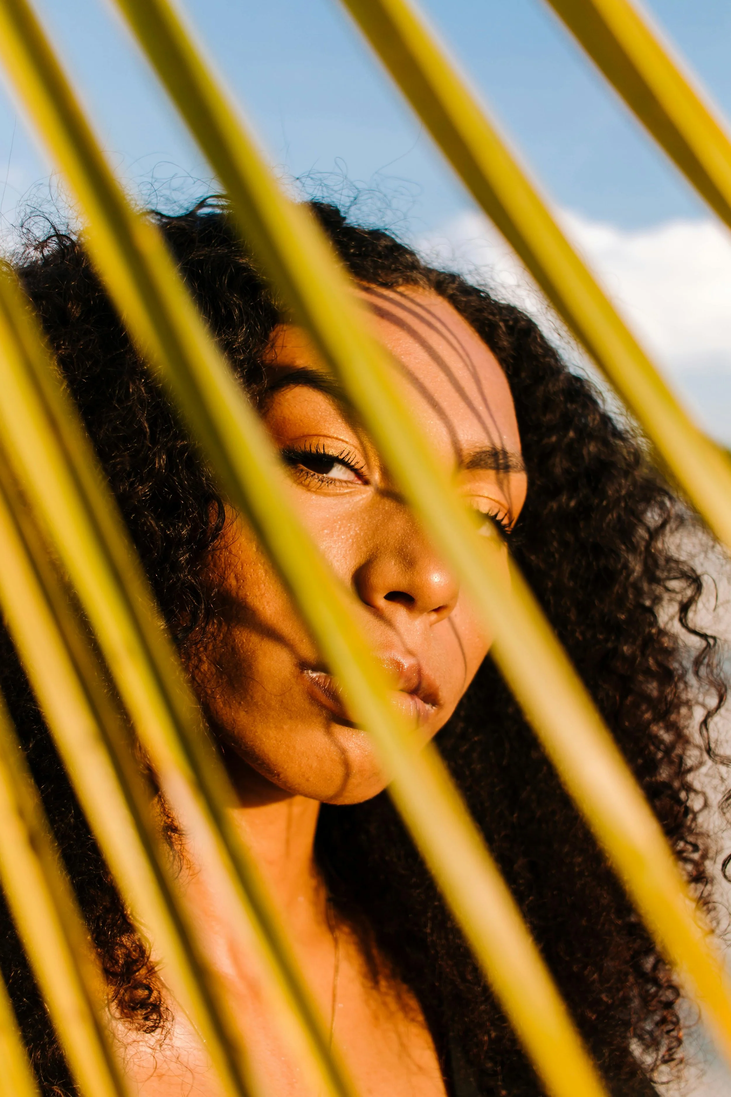 A close-up of a woman with curly hair gazing through yellow intersecting bars.