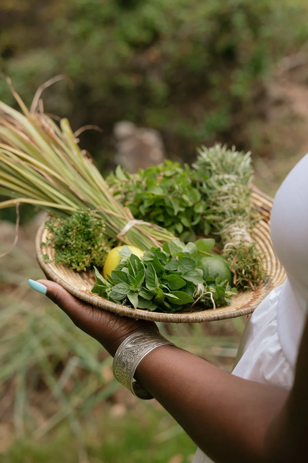 Person holding a woven basket filled with fresh herbs and plants outdoors.