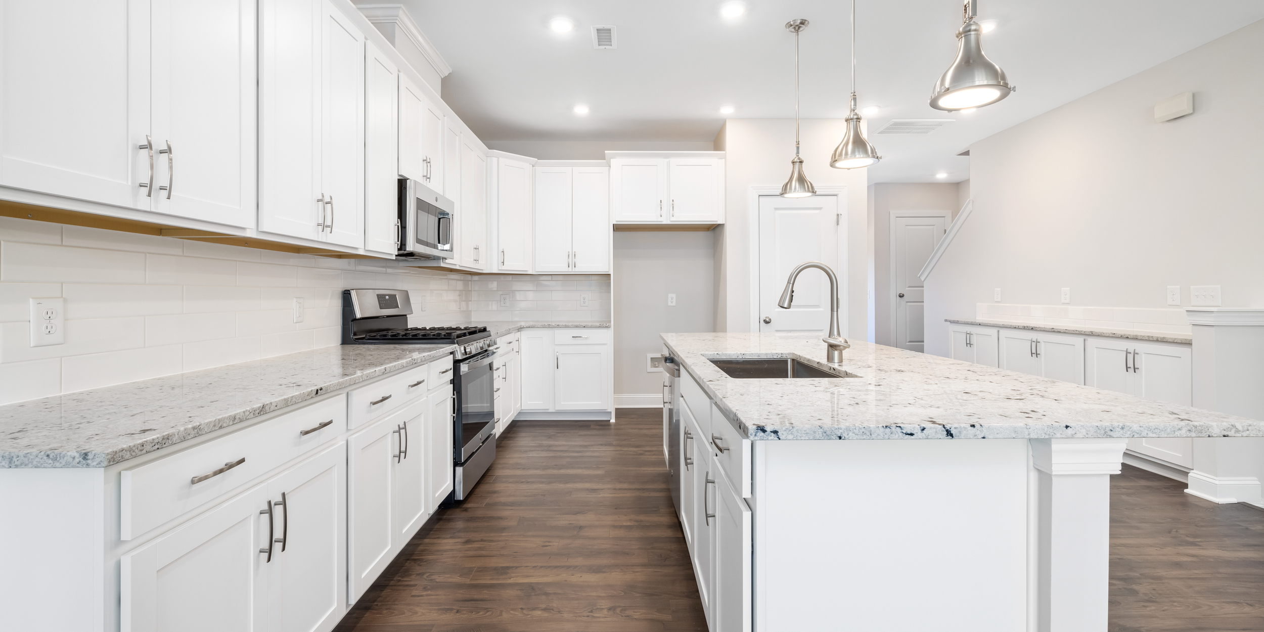 Modern kitchen with white cabinets, granite countertops, stainless steel appliances, and pendant lights over an island.