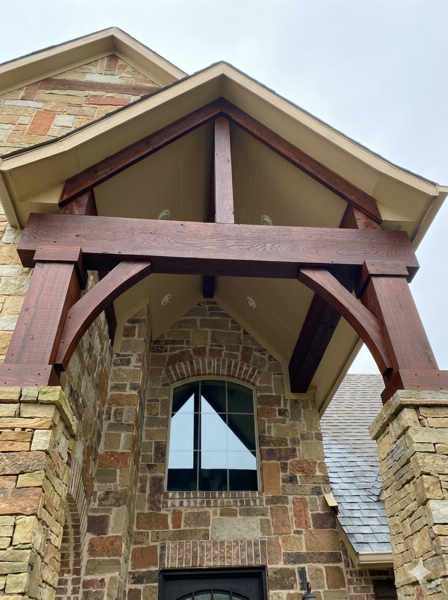 Close-up of a stone and brick house front with a balcony featuring dark wood beams and siding beneath a gabled roof.