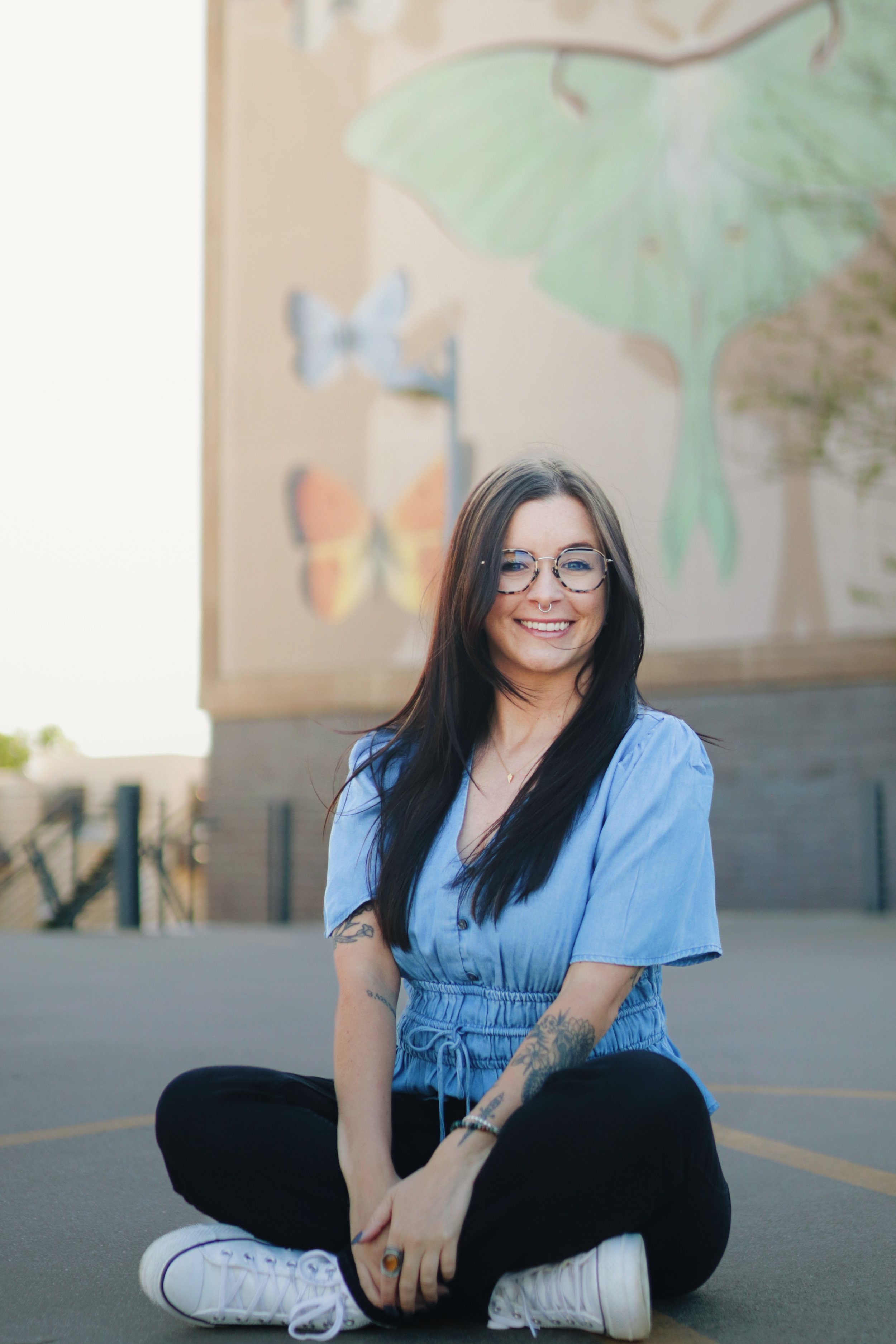Portrait of a queer therapist sitting on a parking garage rooftop with a colorful mural background.