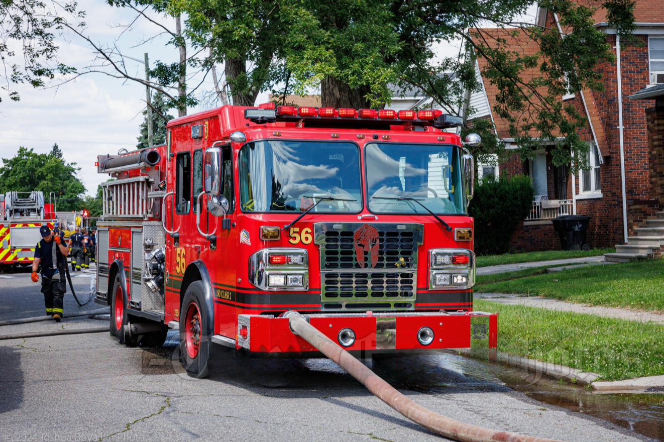 A red fire truck with firefighters working around it on a residential street.