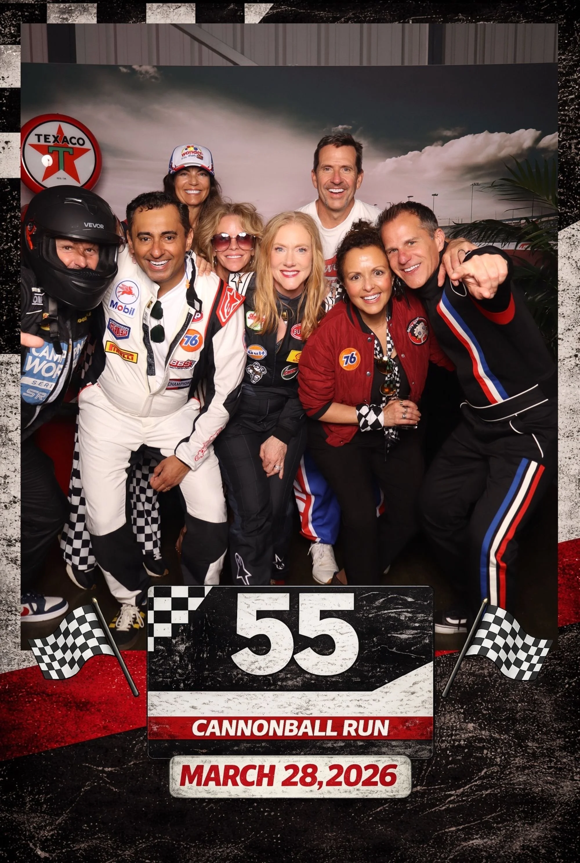 Group of race car drivers and supporters celebrating at the Cannnoball Run event on March 28, 2026, with checkered flags, racing gear, and a backdrop resembling a race track.